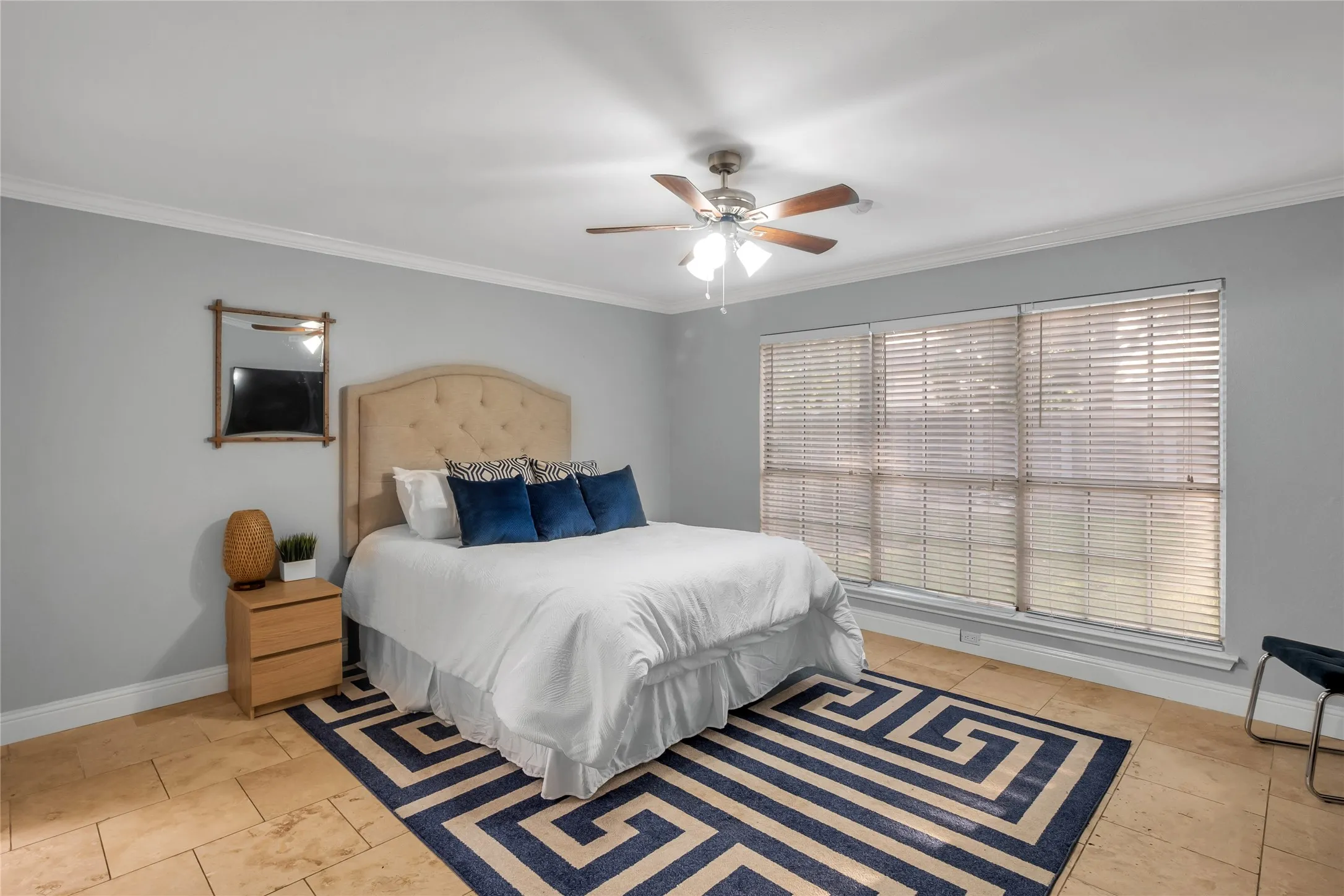 Spacious primary bedroom featuring a wood-finish plank floor, ceiling fan with integrated lighting, arched upholstered headboard, and abundant natural light from triple-panel sliding glass doors with plantation shutters