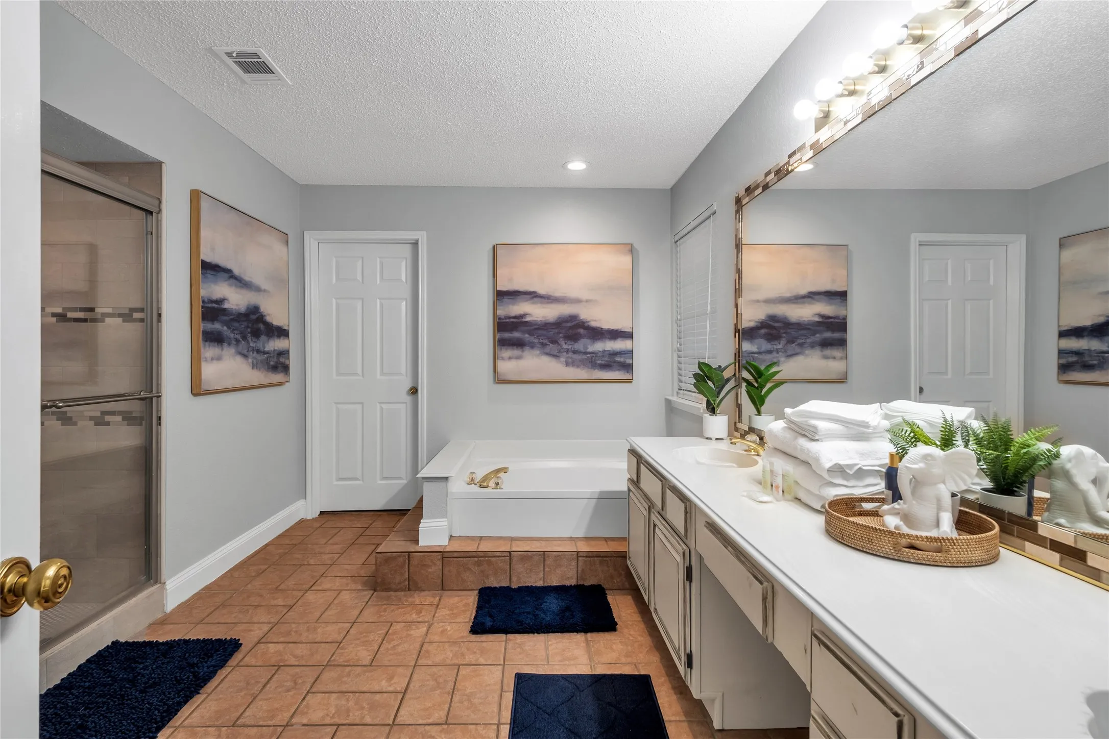 Spacious bathroom featuring a large vanity with ample counter space, built-in soaking tub, walk-in shower with sliding glass door, and tile flooring