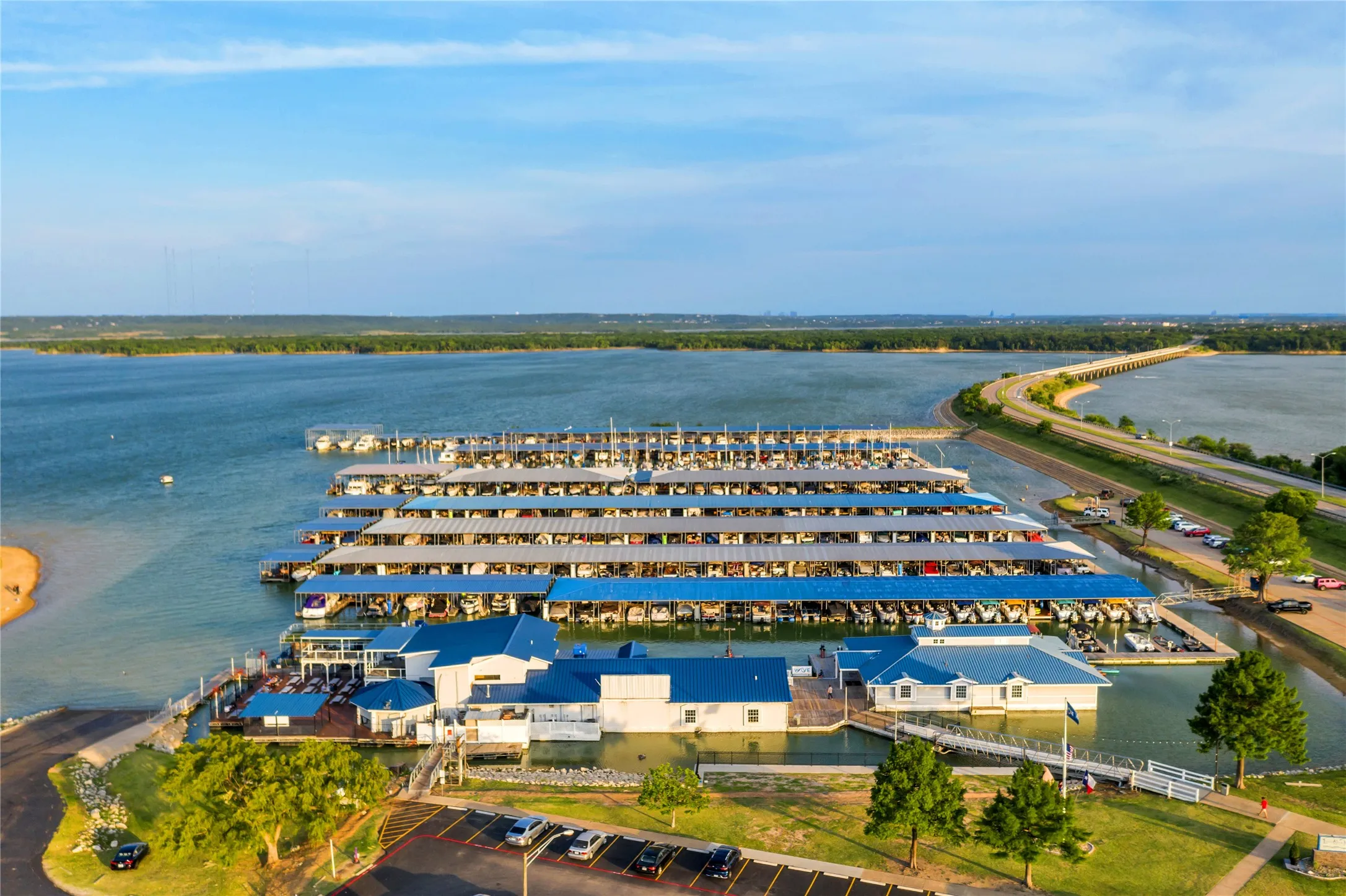 Expansive waterfront property featuring extensive boat slips, multiple dockside structures, a surrounding body of water, a nearby road, and shoreline landscaping