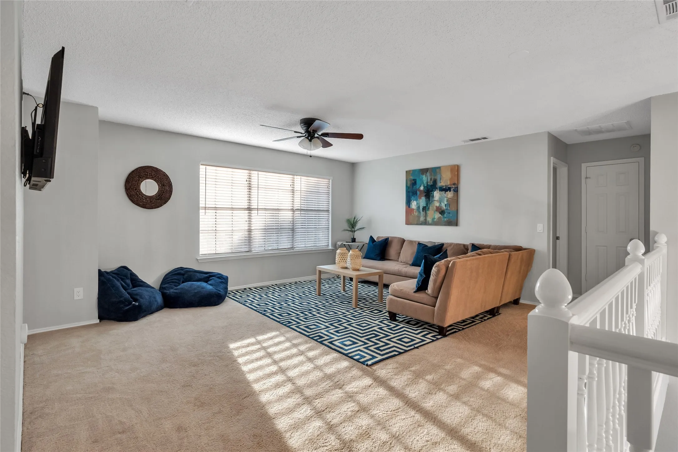 Spacious room with light-colored carpeting, large windows with blinds, and a ceiling fan