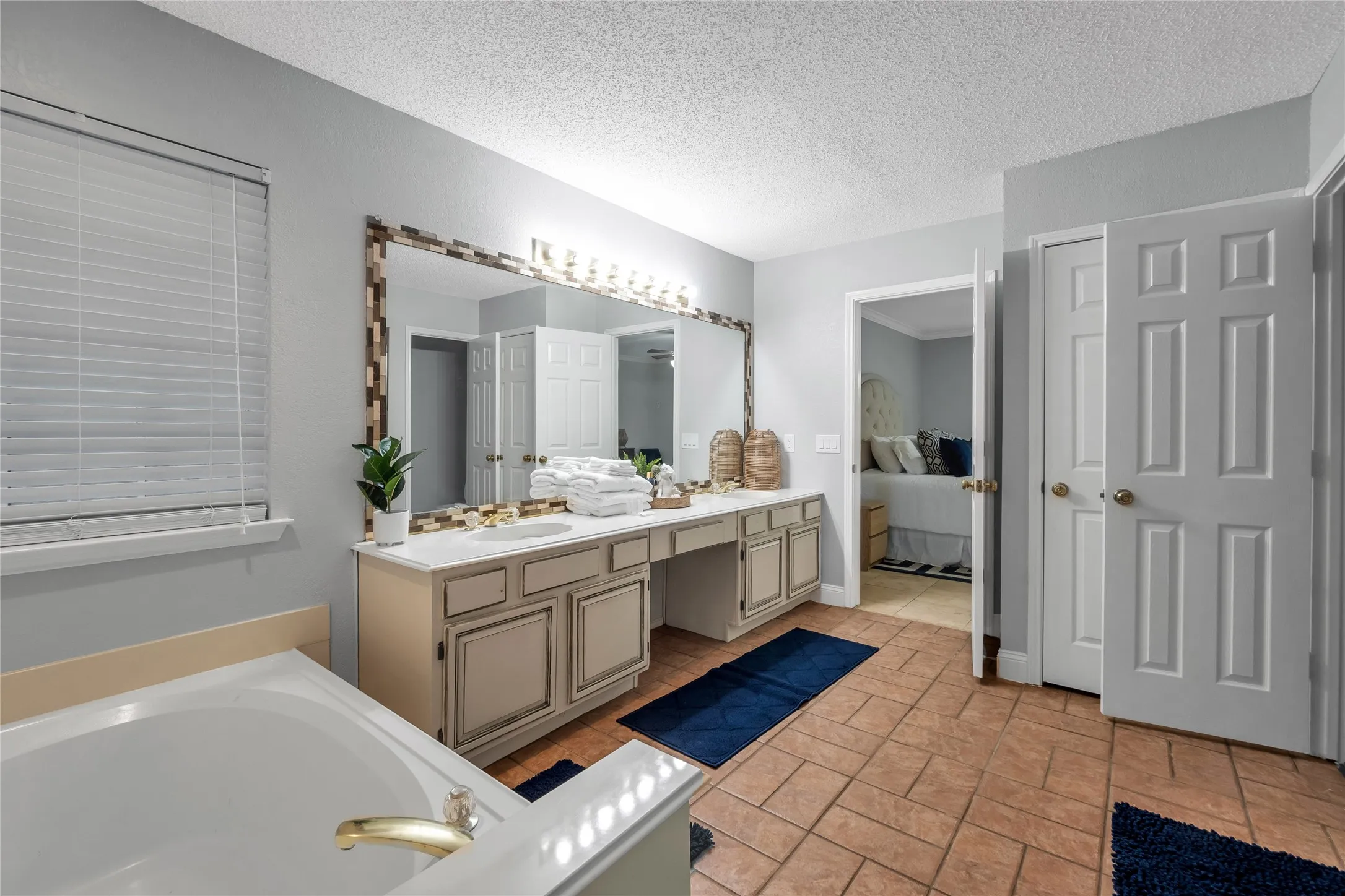 Dual vanity with integrated sinks, large framed mirror, built-in cabinetry, and a soaking tub with brass fixtures