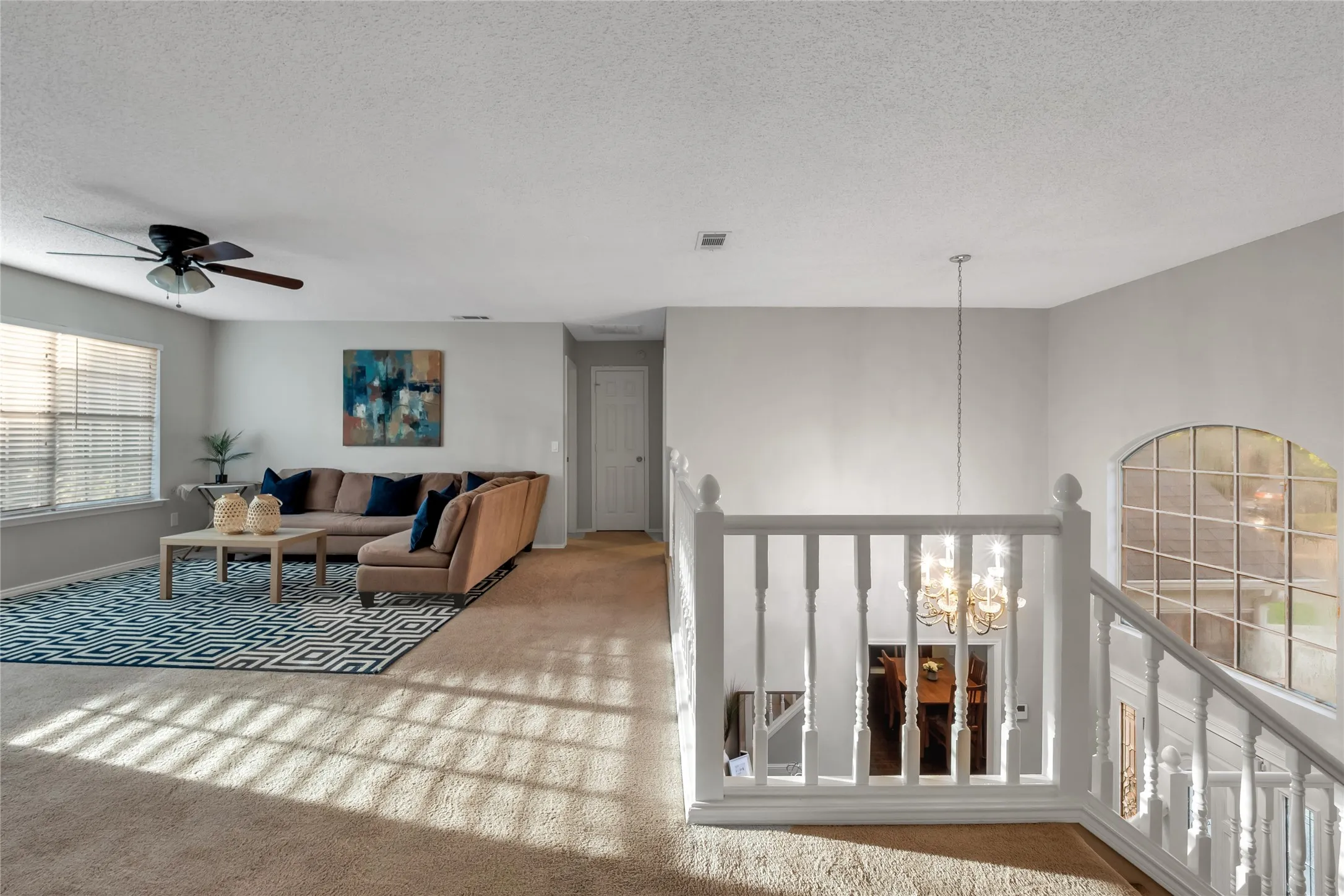 Carpeted flooring, ceiling fan, white paneled door, and a white staircase with a chandelier
