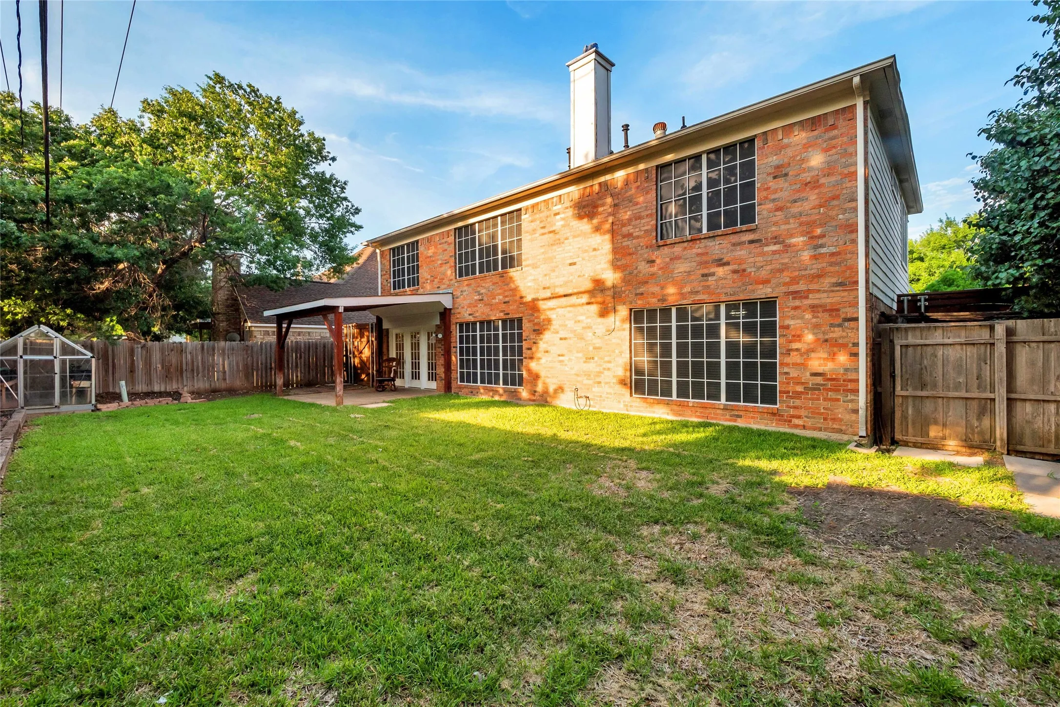 Brick exterior with multiple pane windows, ground-level covered patio with wood supports, and an expansive lawn
