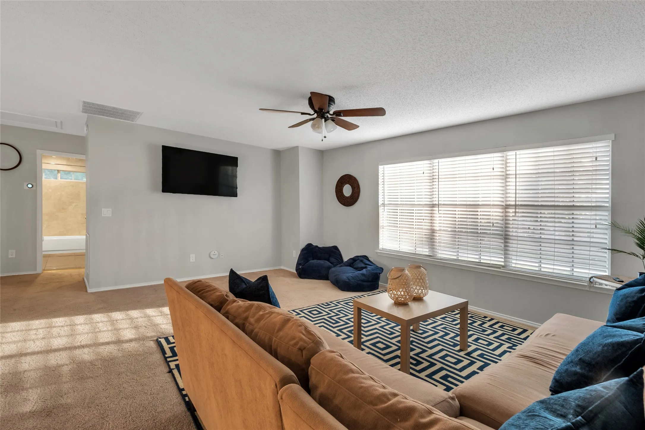 Expansive living area featuring carpeted flooring, a ceiling fan, and multiple windows with blinds
