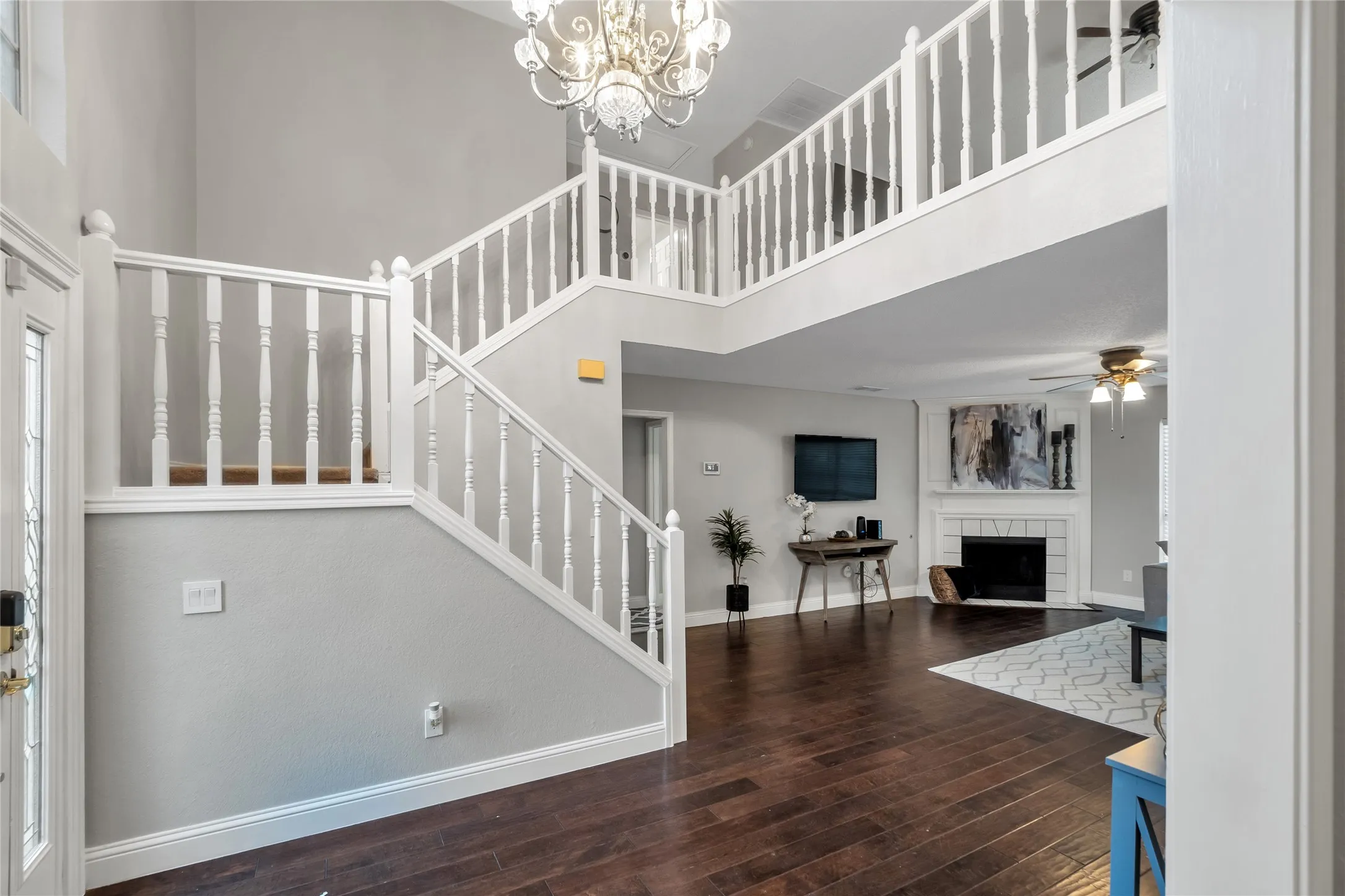 Two-story entryway with wood-finish flooring, white spindle staircase, and a decorative chandelier