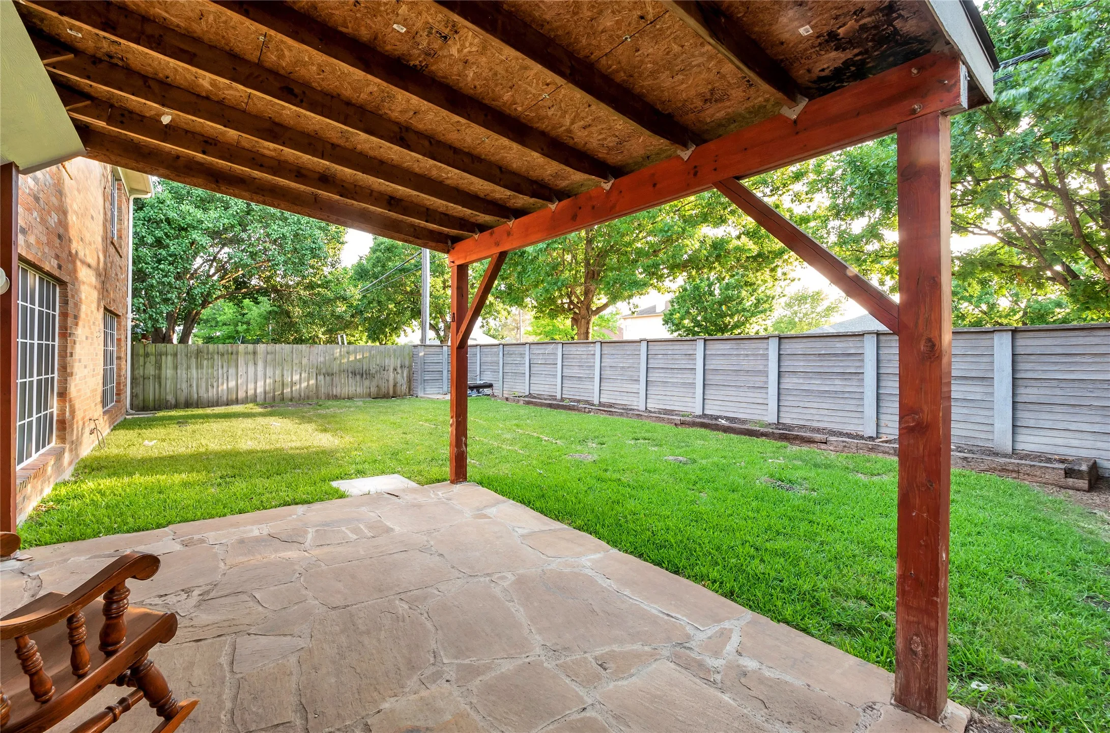 Covered patio with flagstone flooring, bordered by a green lawn and privacy fencing