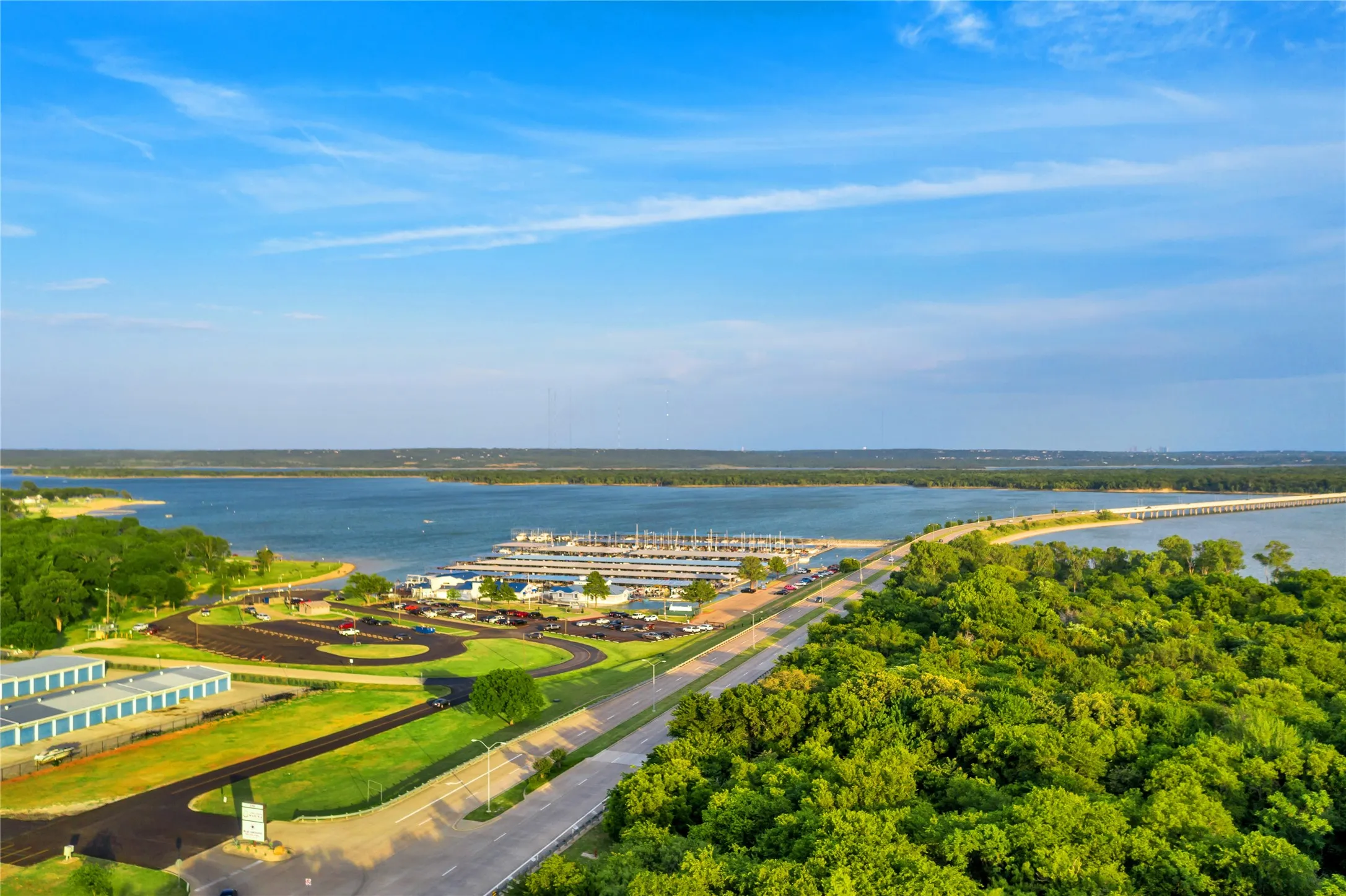 Expansive waterfront featuring a marina with numerous boat slips, a paved roadway, and extensive natural tree coverage