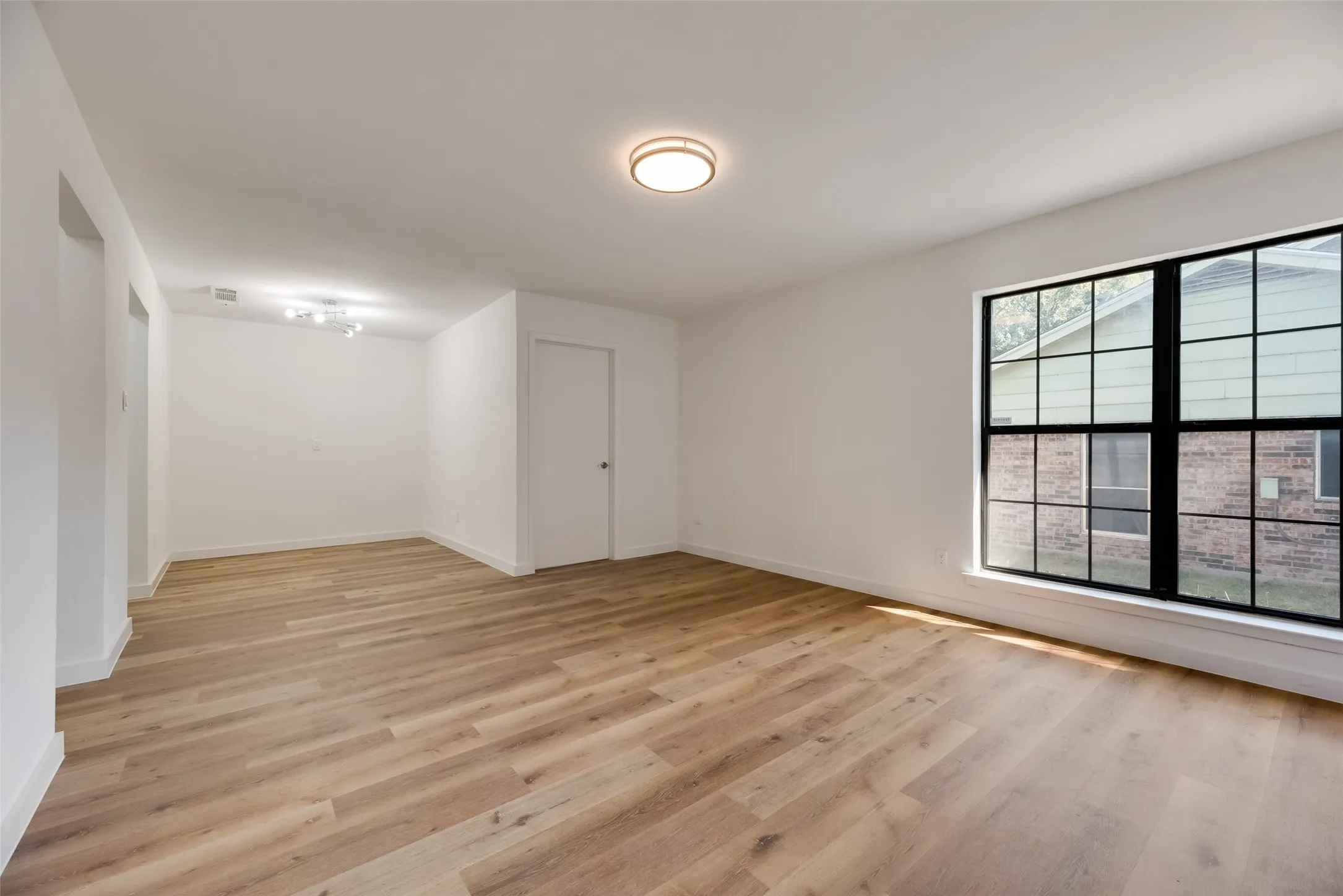 Light wood-finish flooring, white painted walls, and a large window with black grid framing