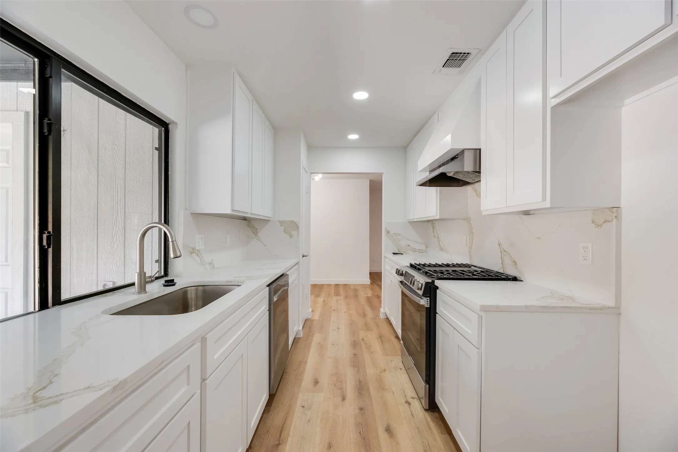 Galley kitchen featuring white cabinetry, light countertops, stainless steel appliances, wood-finish flooring, and recessed lighting