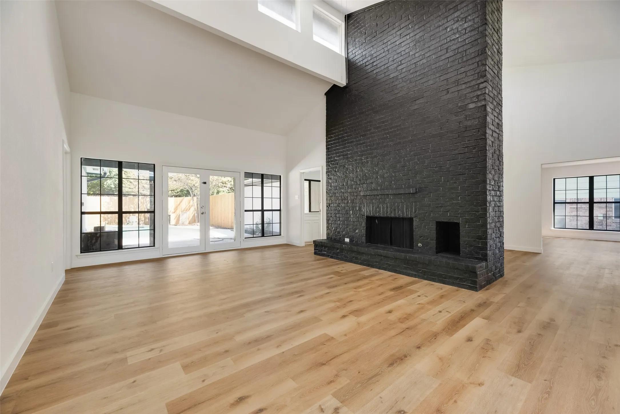 Vaulted ceilings, wood-finish flooring, a black brick fireplace, and large windows with black frames
