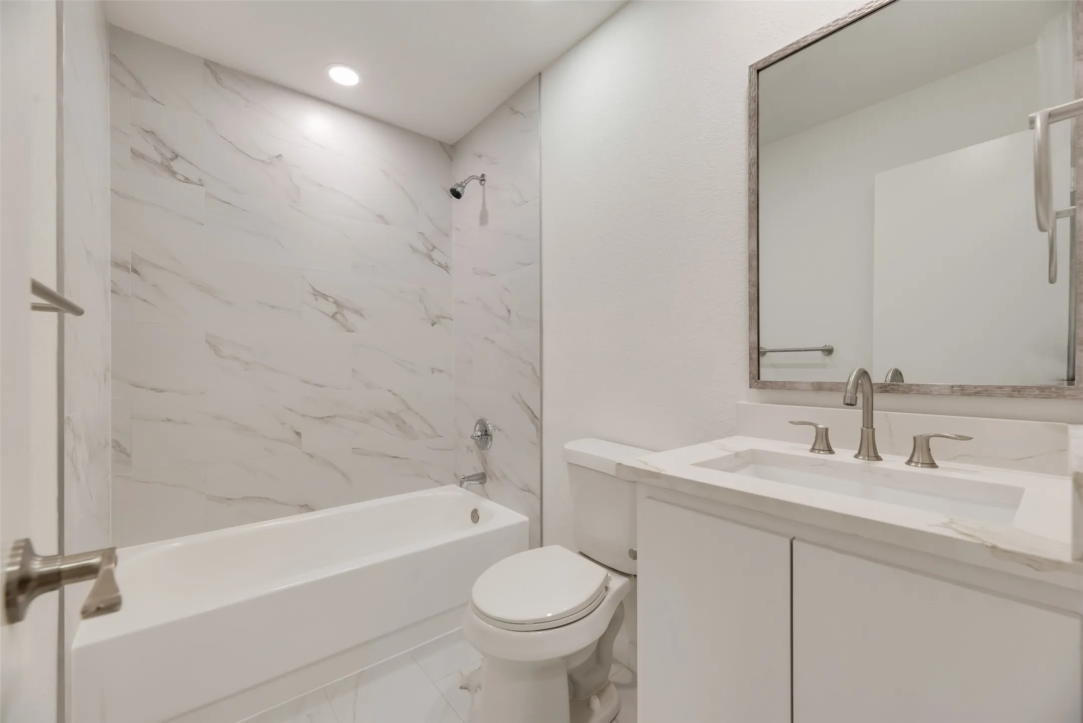 Bathtub with shower, white vanity cabinet with countertop, integrated sink, and framed wall mirror