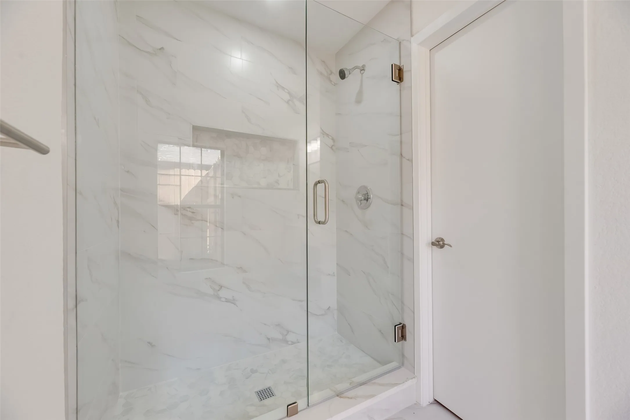 Glass-enclosed shower with white marble-look tile, built-in shower niche, and a contrasting shower floor
