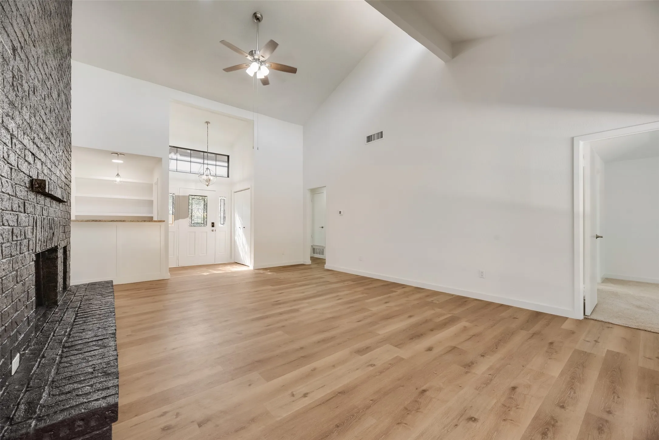 Vaulted ceiling featuring exposed beams, wood-finish flooring, brick fireplace, and built-in shelving