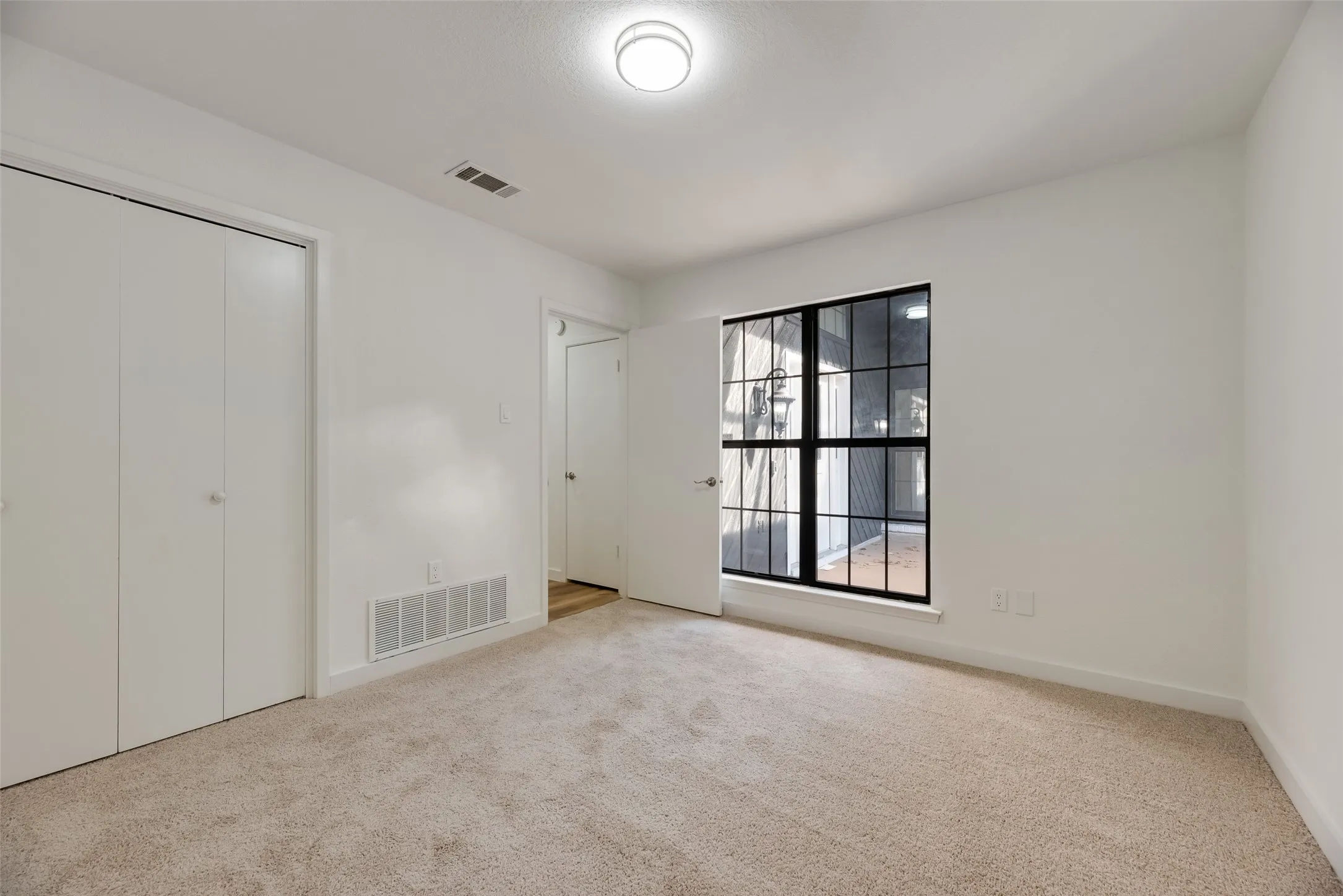 Carpet flooring, white walls, bi-fold closet doors, ceiling-mounted light fixture, and a window with black grid panes
