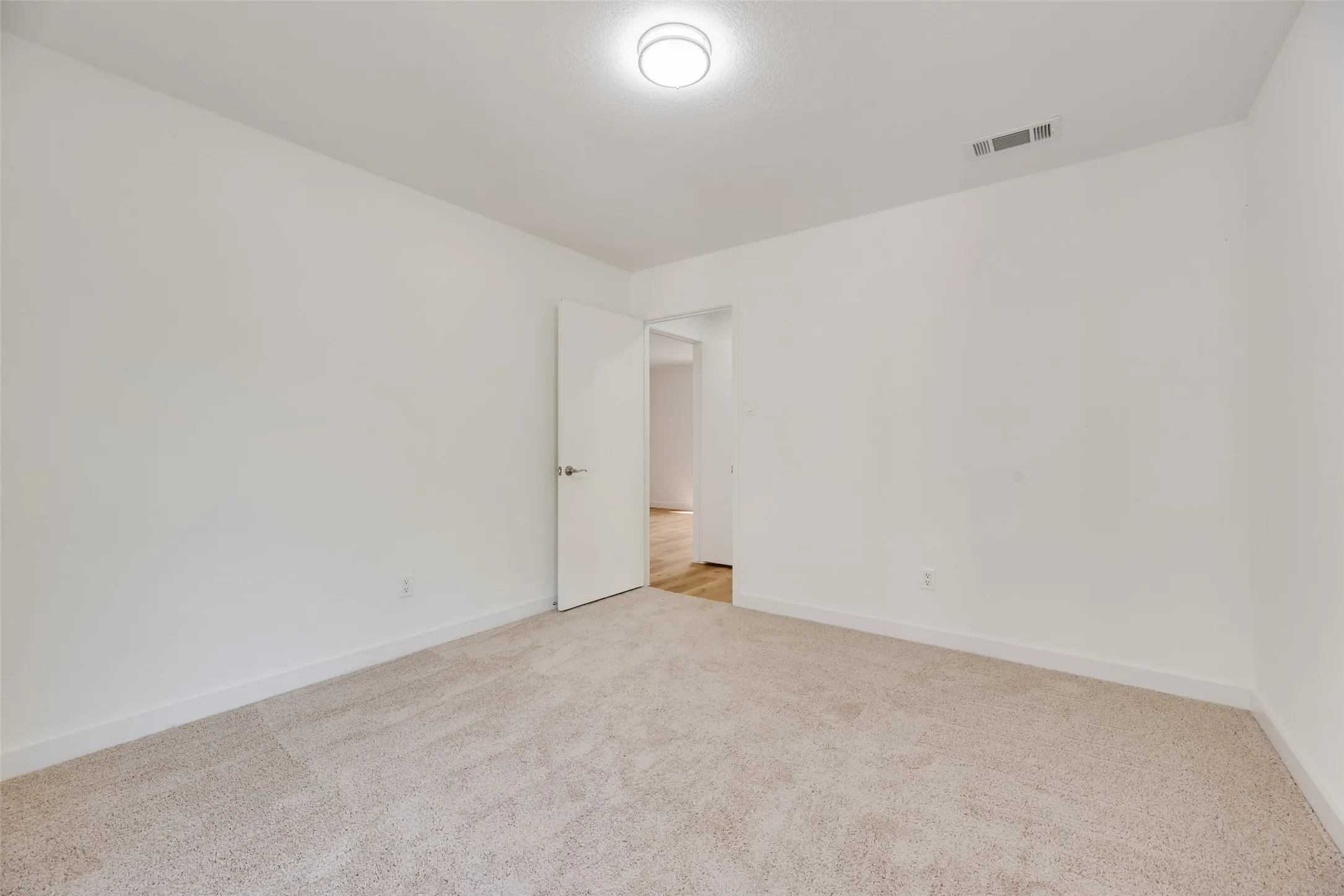 Wall-to-wall carpeting, bright white walls, flush mount ceiling light fixture, and a solid core door