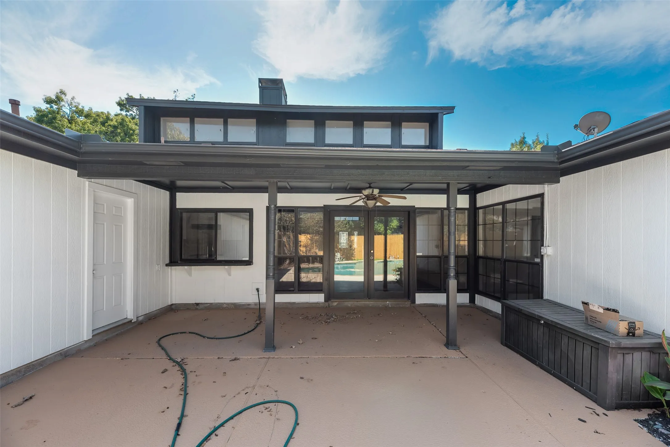 Exterior patio featuring a covered area with a ceiling fan, multiple windows, and a white paneled door