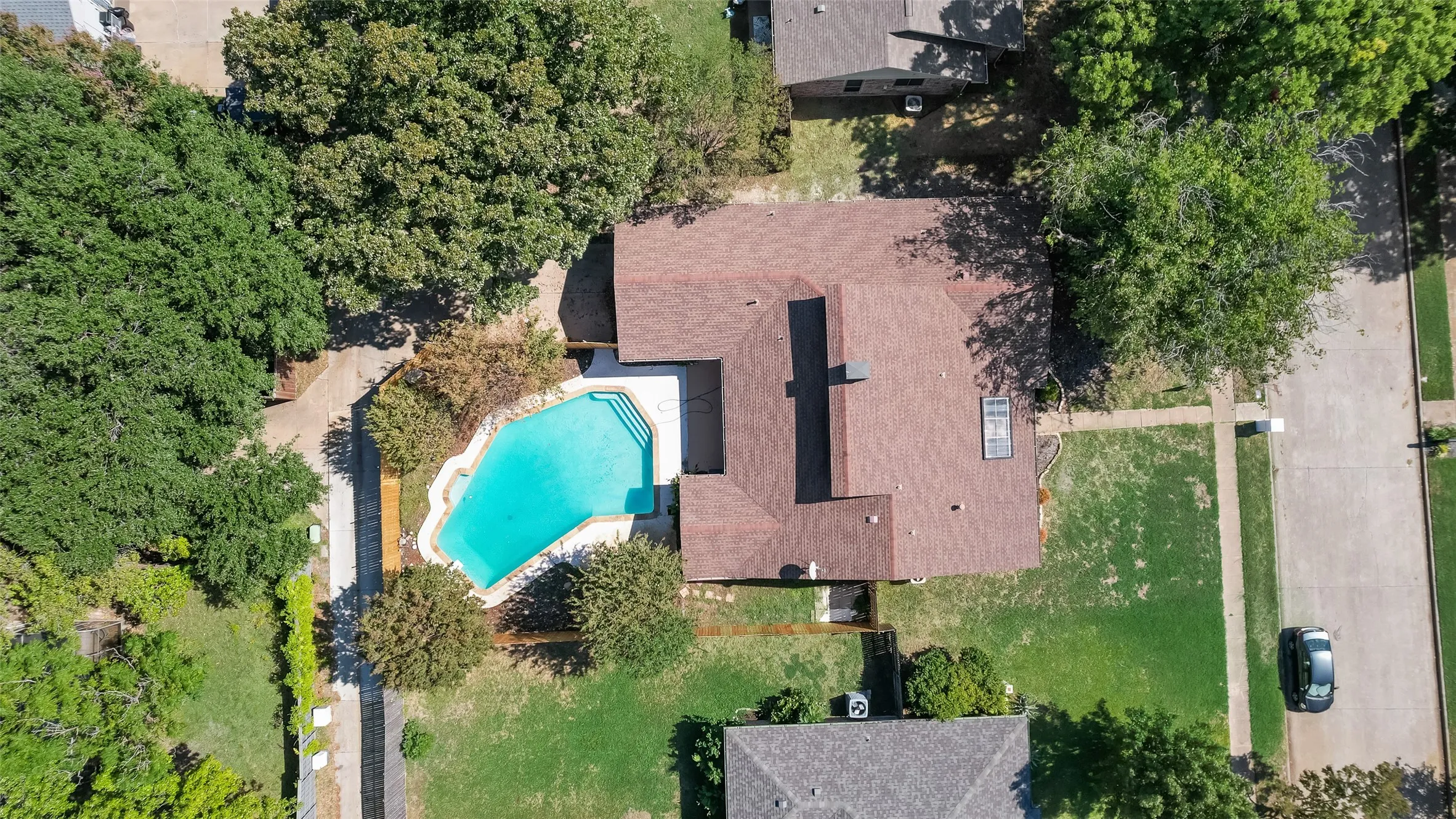 Irregularly shaped pool with integrated steps, surrounding hardscaping, and a mature tree canopy