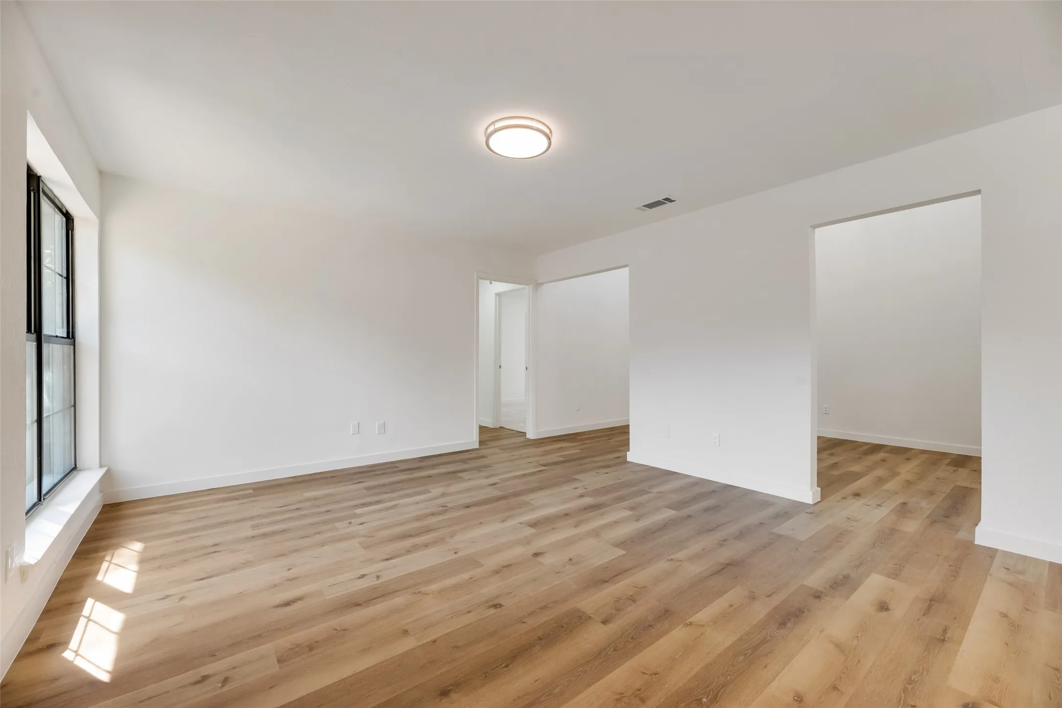 Recessed ceiling light, white walls, wood-finish flooring, black window frames, and open doorways