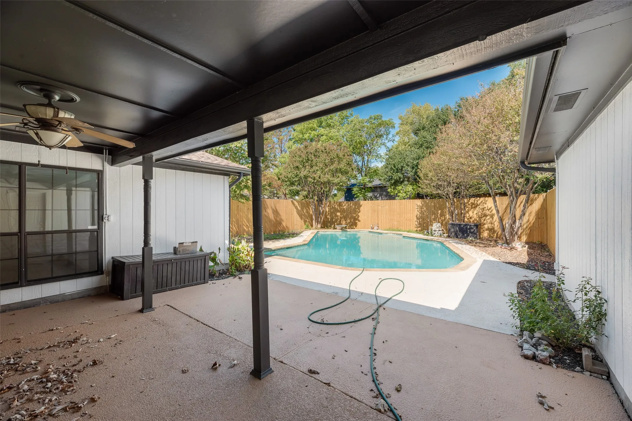 Covered patio with a ceiling fan, leading to a fenced backyard featuring an in-ground swimming pool and mature trees