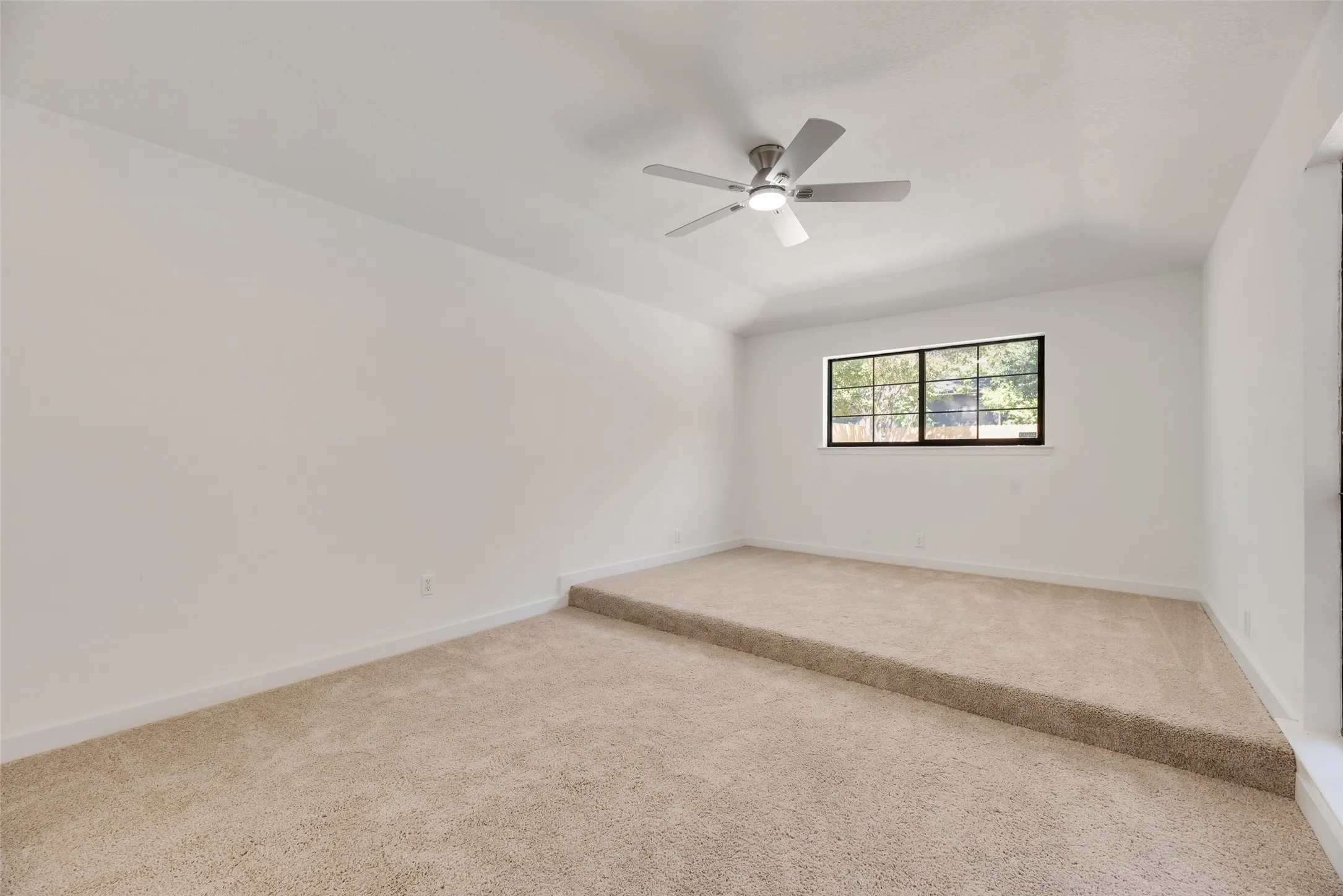 Vaulted ceiling with an installed ceiling fan, neutral wall paint, and beige carpet