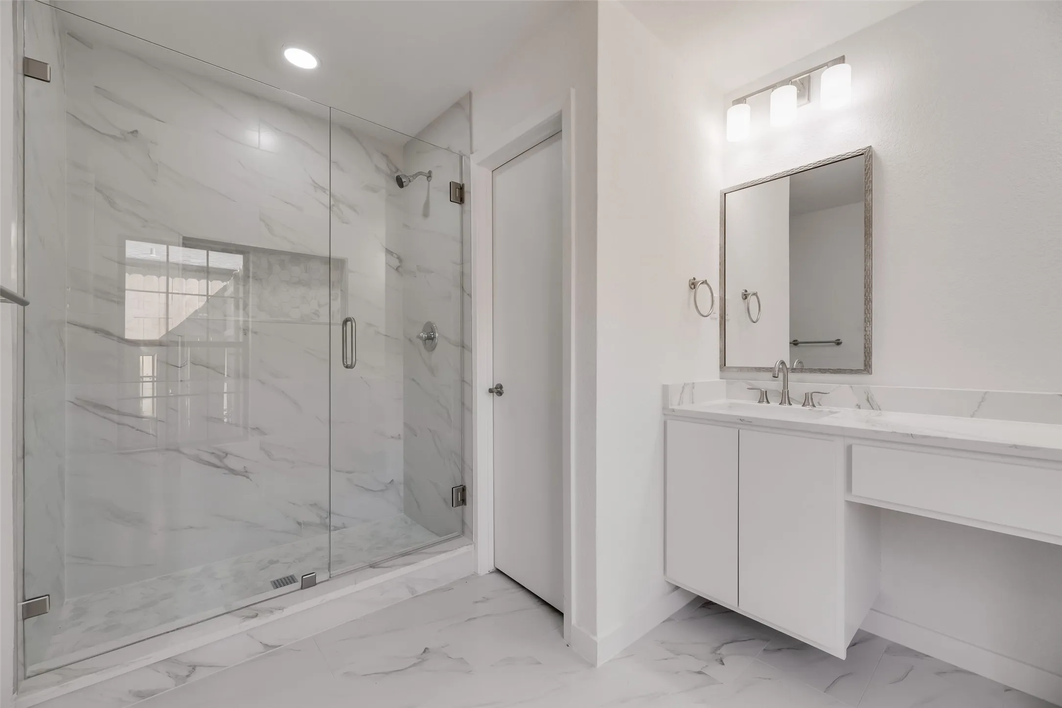 Walk-in shower with clear glass enclosure and marble-look tile