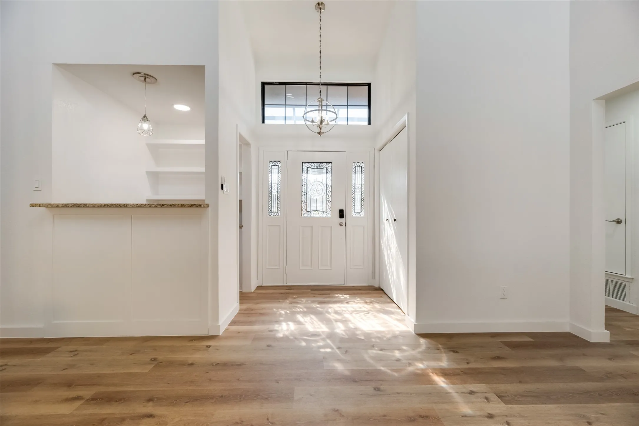 Wood-finish flooring, white double entry doors, transom window, vaulted ceiling, and a built-in countertop with shelving