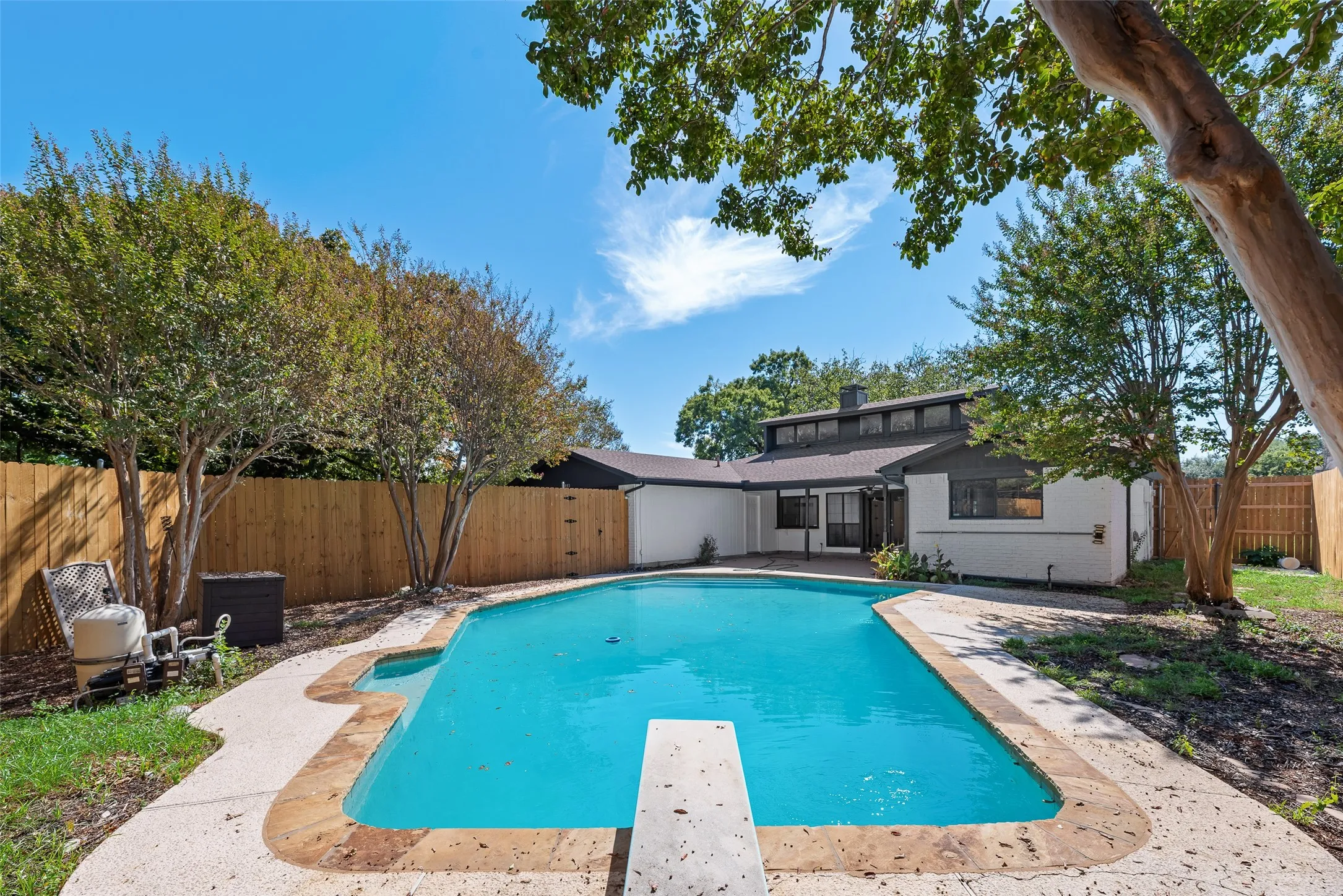 Private backyard with a rectangular swimming pool featuring a diving board, surrounding concrete patio, and mature trees