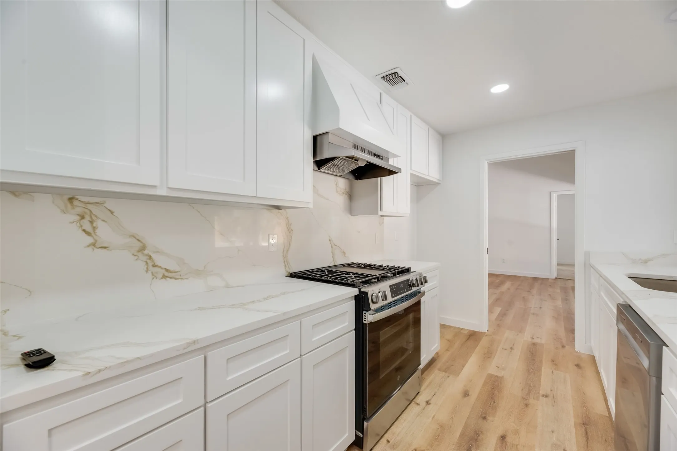 White shaker-style cabinetry, stainless steel range, white countertops with veining, matching backsplash, and light wood-finish flooring