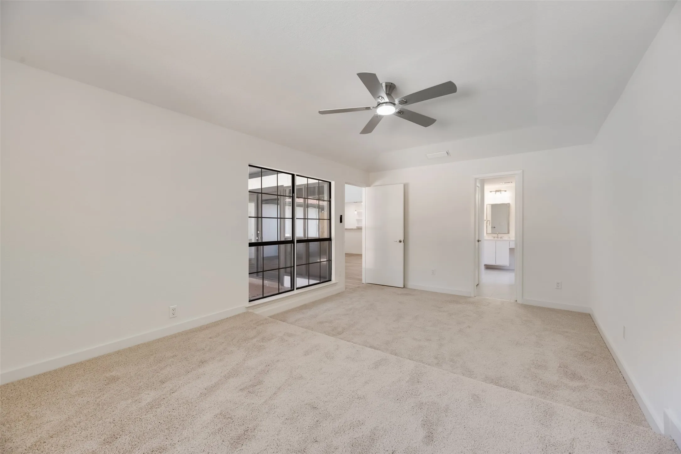 Spacious room with carpet flooring, a multi-pane window, and a contemporary ceiling fan