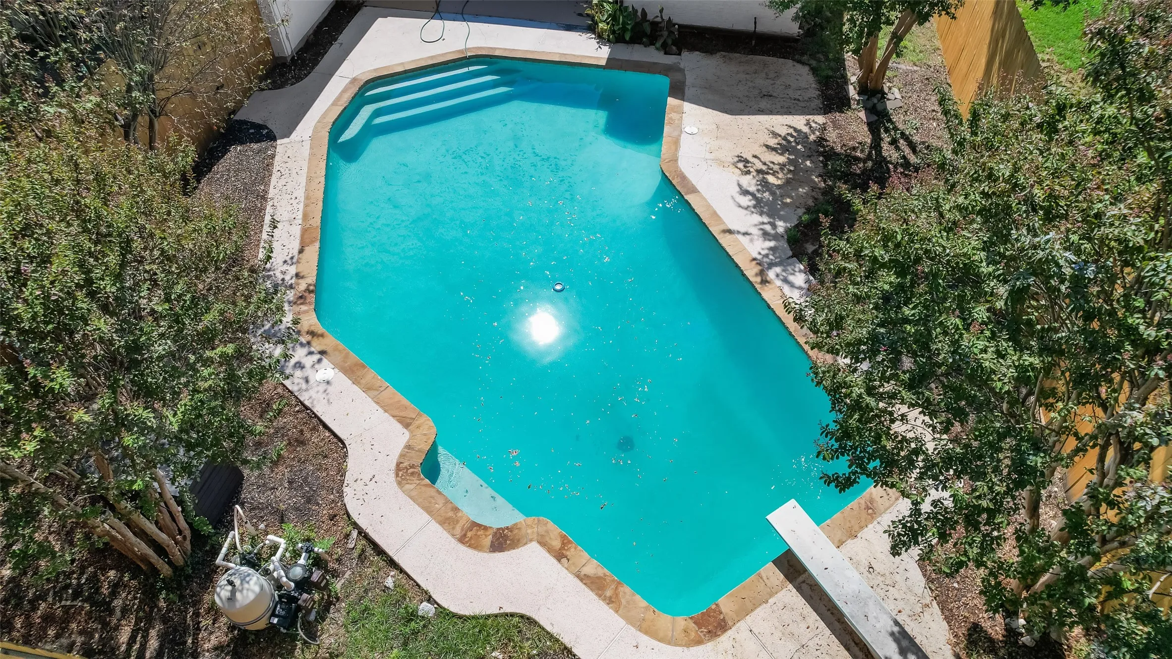 Outdoor swimming pool with concrete decking, integrated steps, and a diving board