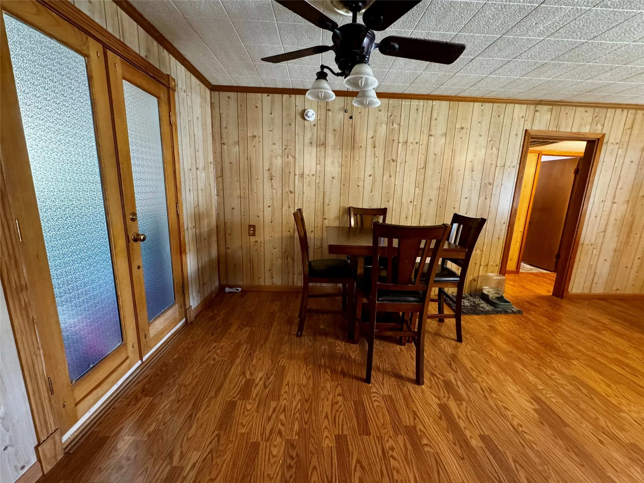 Wood-finish flooring, paneled walls, and a ceiling fan with integrated lighting