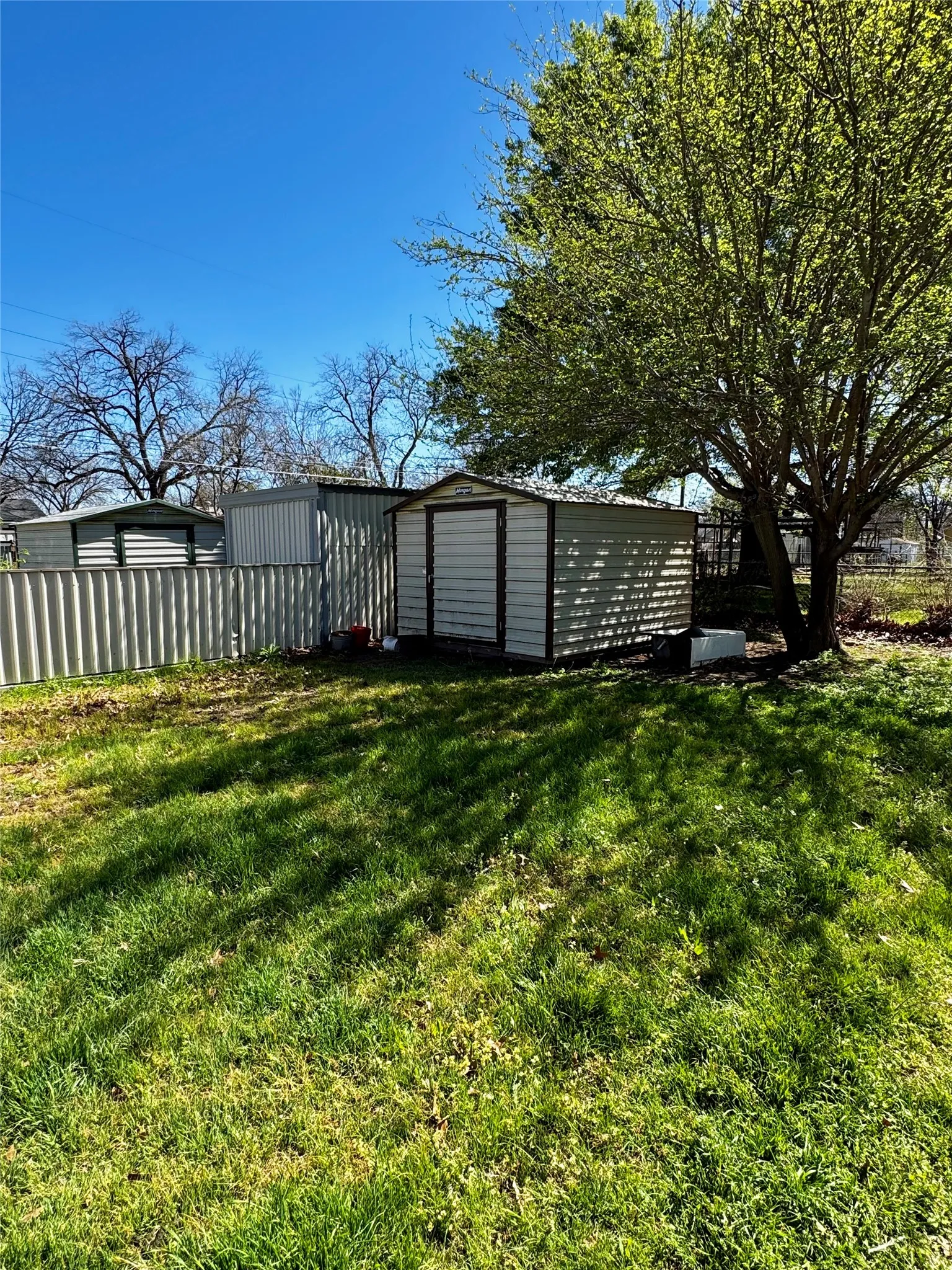Expansive yard space featuring a mature tree, two storage sheds, and a privacy fence