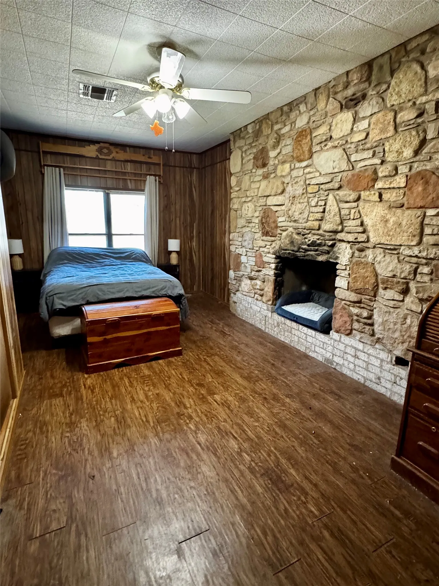 Stone accent wall featuring an integrated fireplace, wood-finish flooring, wood paneling, and a ceiling fan