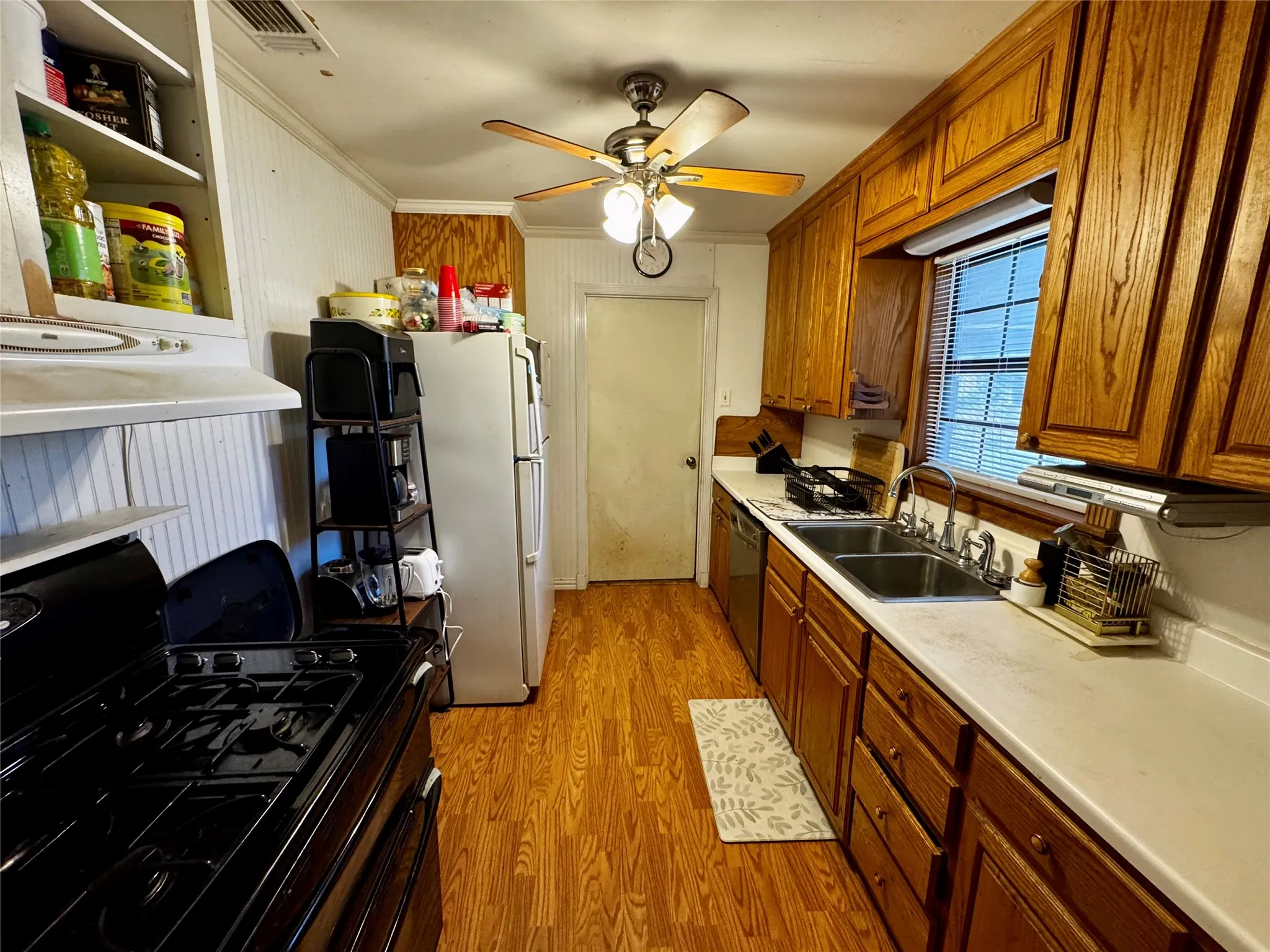 Full kitchen featuring wood-finish flooring, abundant wood cabinetry, a dual basin stainless steel sink, and light-toned countertops