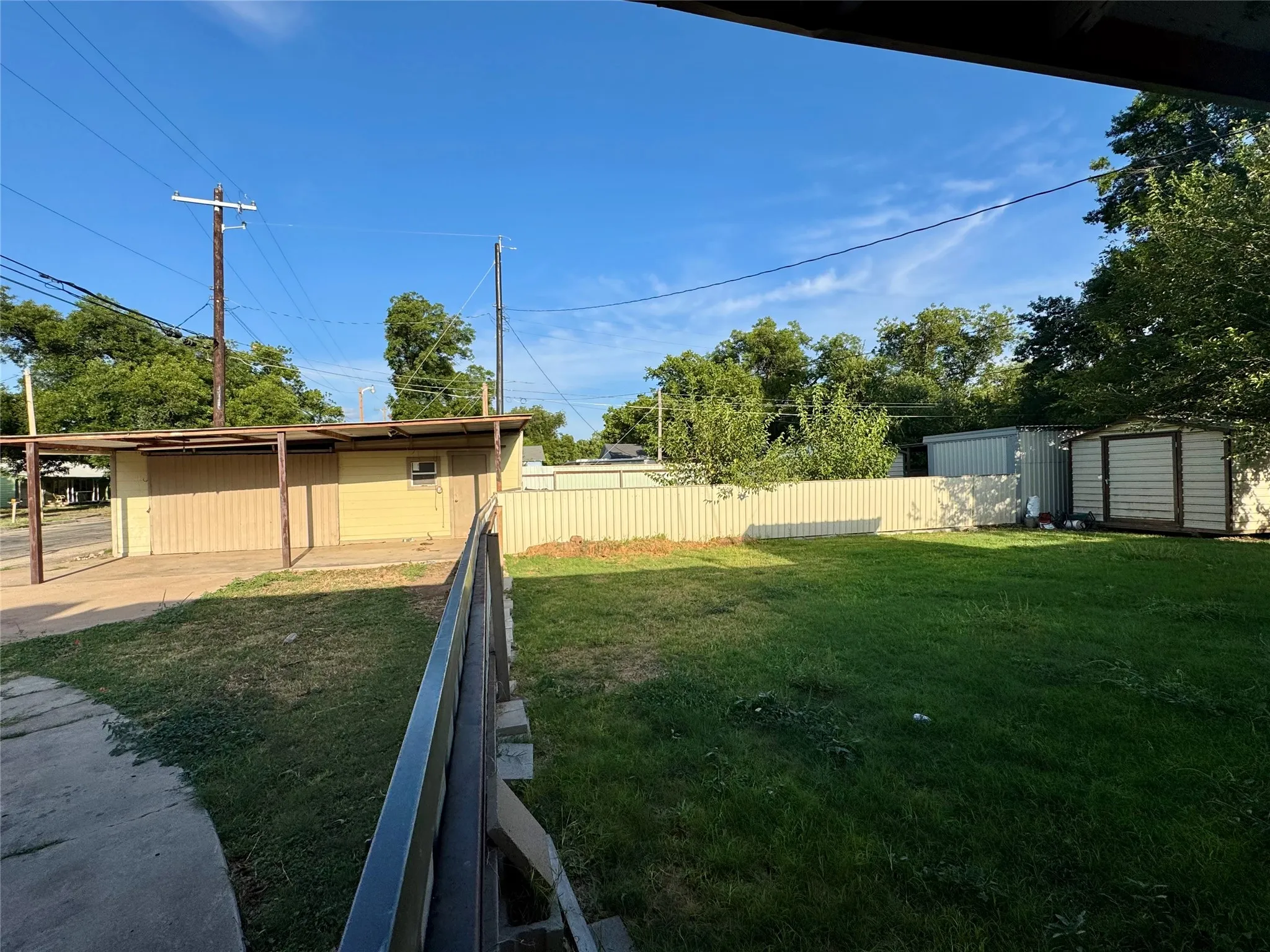 Expansive grassy yard with a privacy fence, two storage sheds, and mature perimeter trees