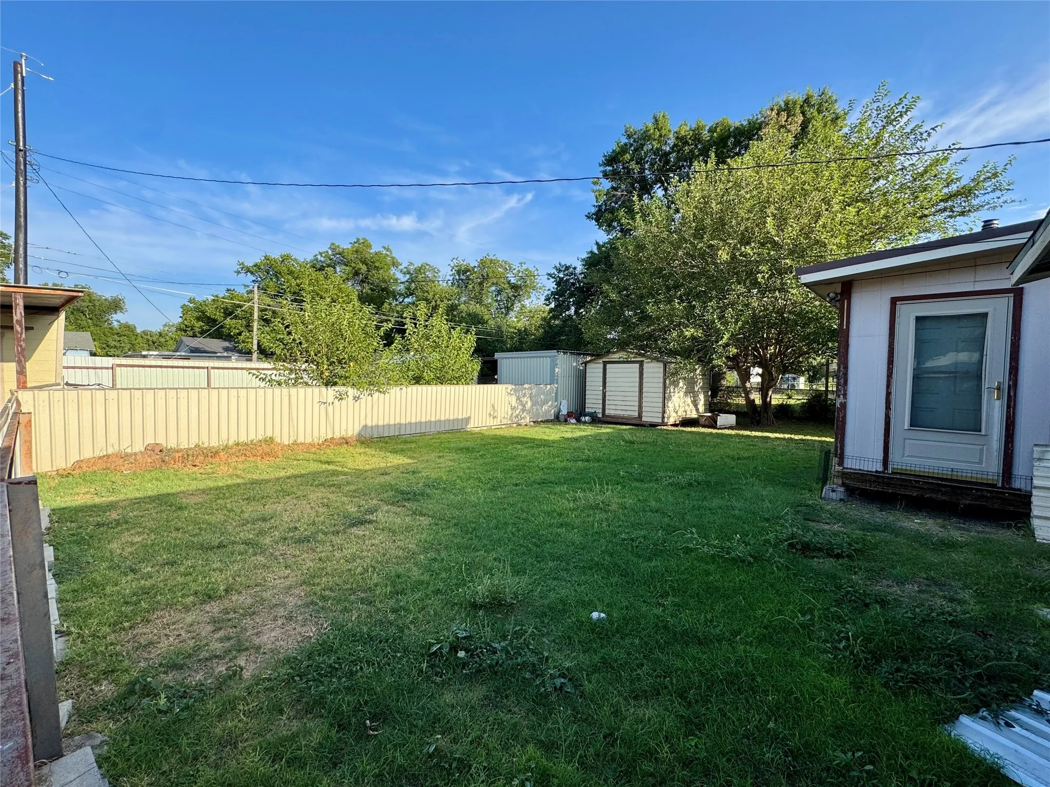 Expansive rear yard featuring a metal fence, mature trees, and a utility shed
