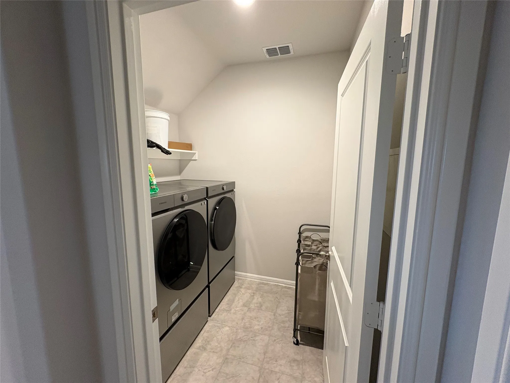 Dedicated laundry area featuring a sloped ceiling, light-toned flooring, and a white wall shelf