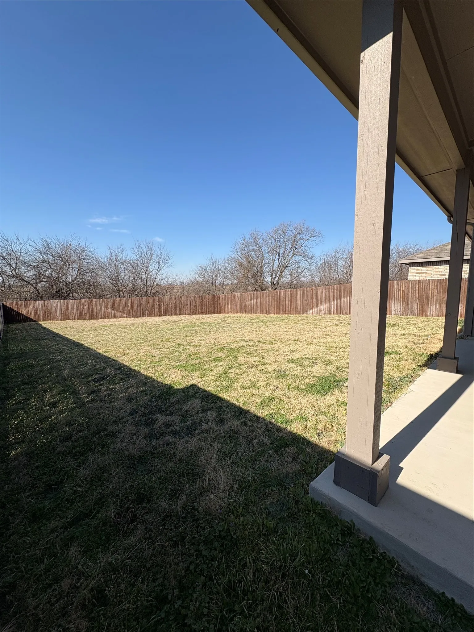 Expansive outdoor area featuring a wide grass lawn, full privacy fencing, and a covered patio with concrete flooring