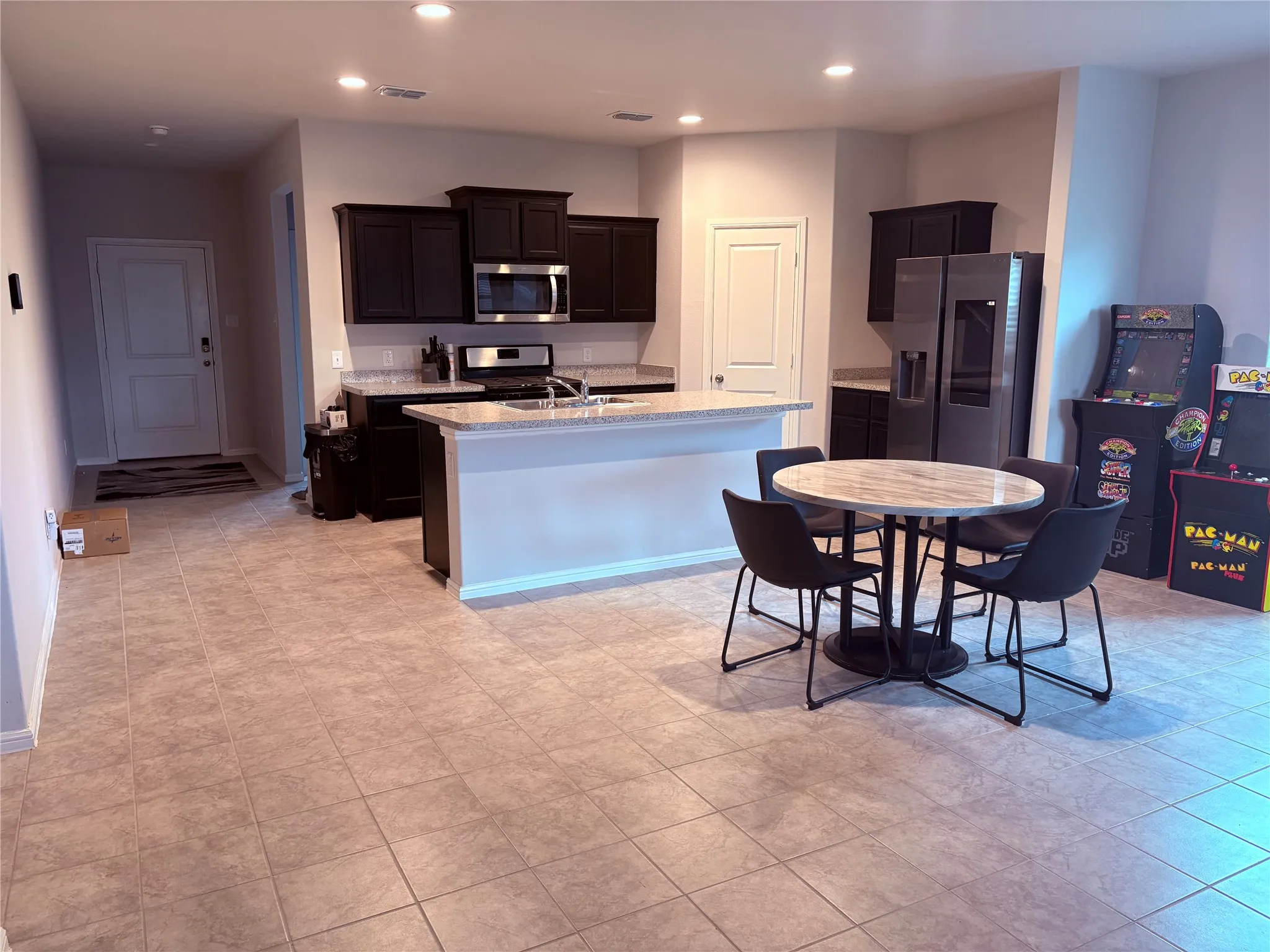 Open-concept kitchen featuring dark wood cabinetry, stainless steel appliances, granite-look countertops, and a central island with a breakfast bar