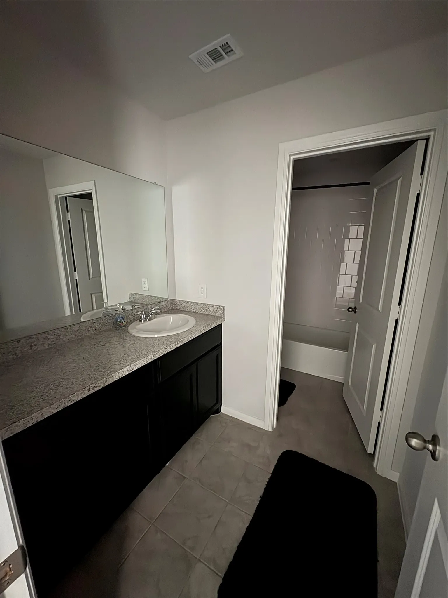 Bathroom featuring a dark wood finish vanity with a light speckled countertop, undermount sink, and large wall-mounted mirror
