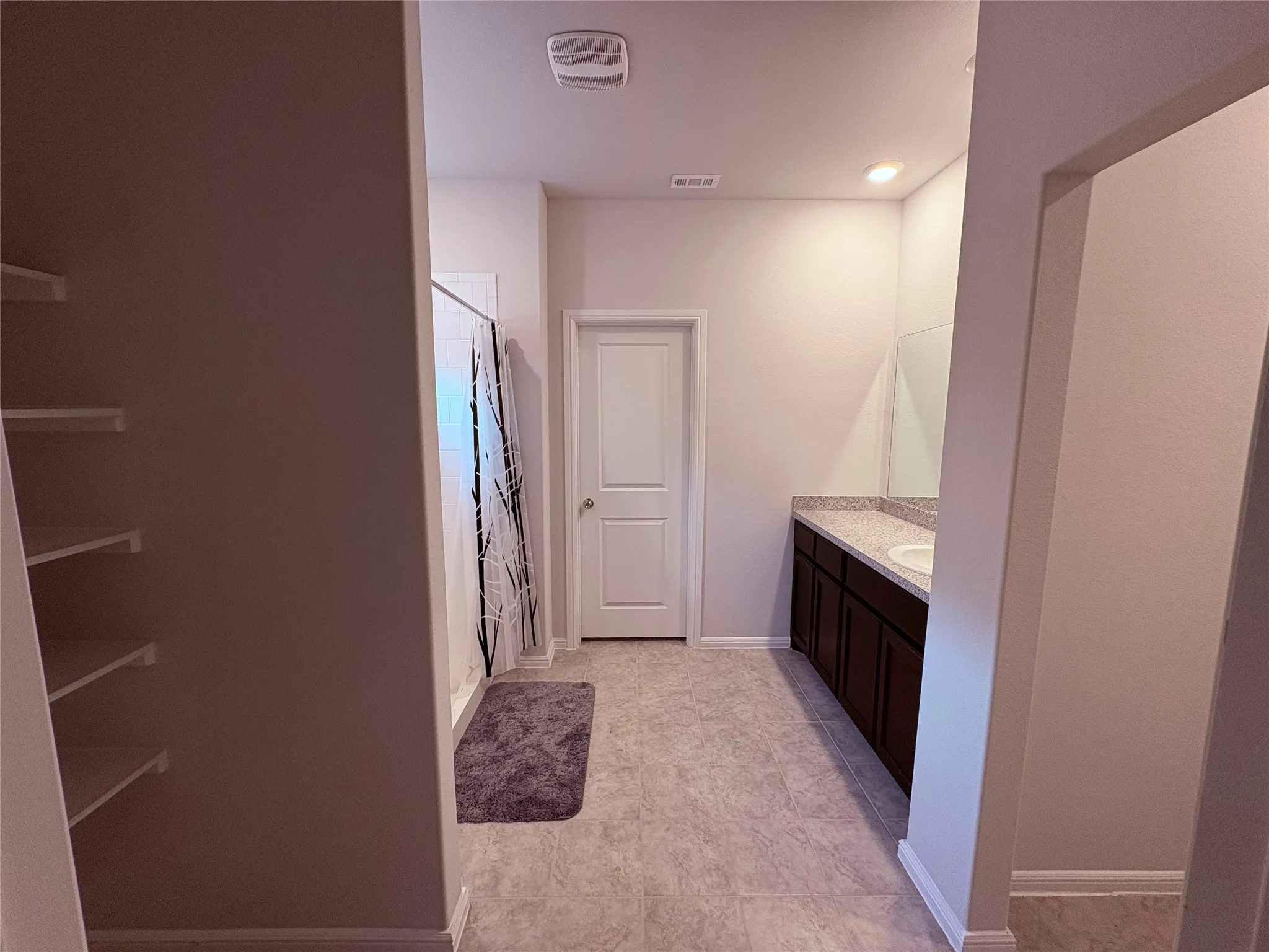Built-in shelving, tile flooring, shower enclosure, vanity with integrated sink, and a large wall mirror