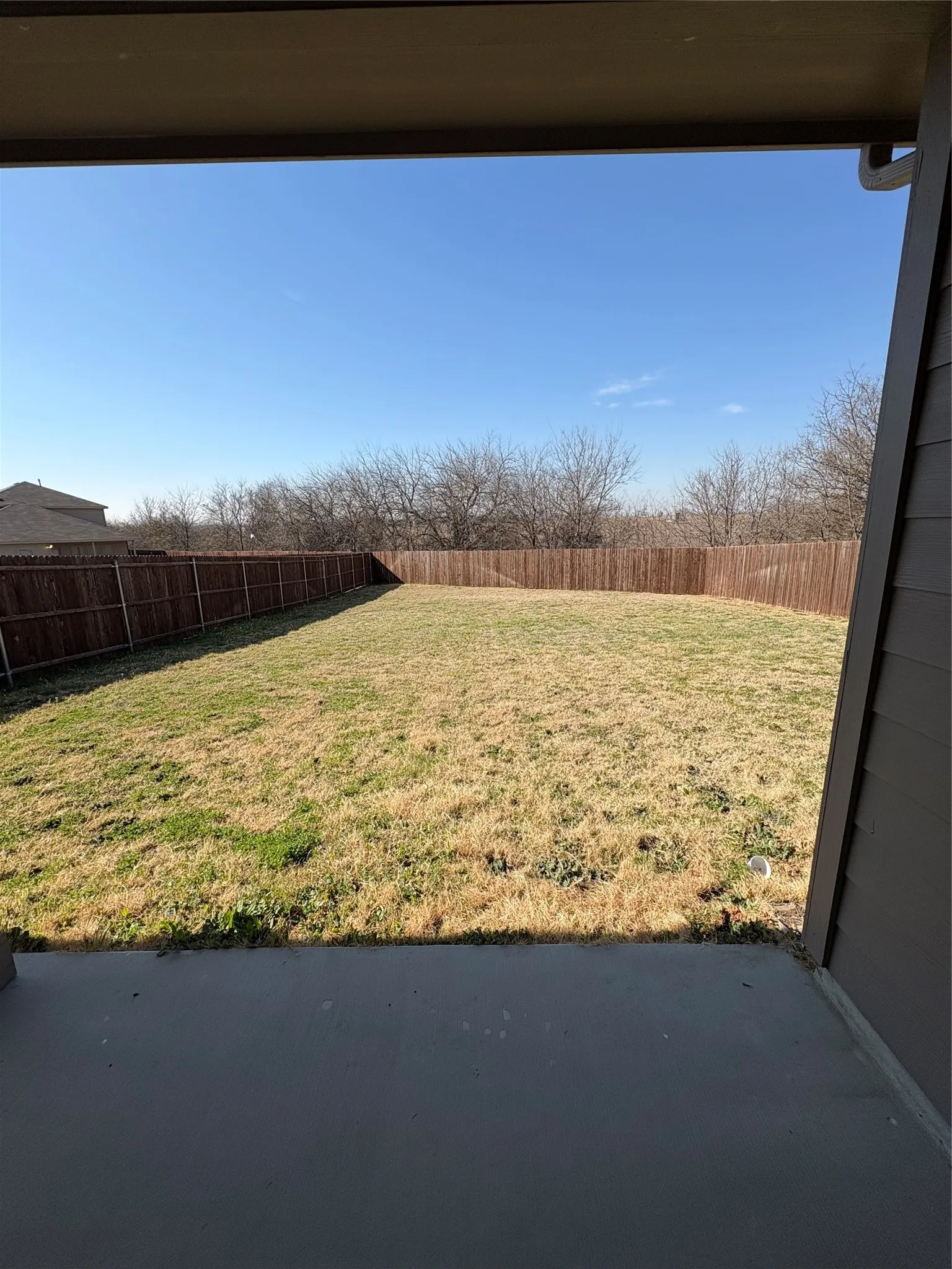 Expansive backyard with a full privacy fence and a concrete patio