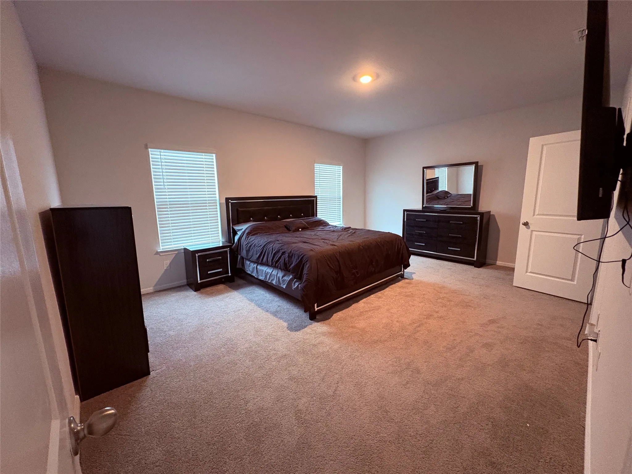 Recessed lighting, neutral wall tones, two windows with blinds, light brown carpet flooring, and a white interior door