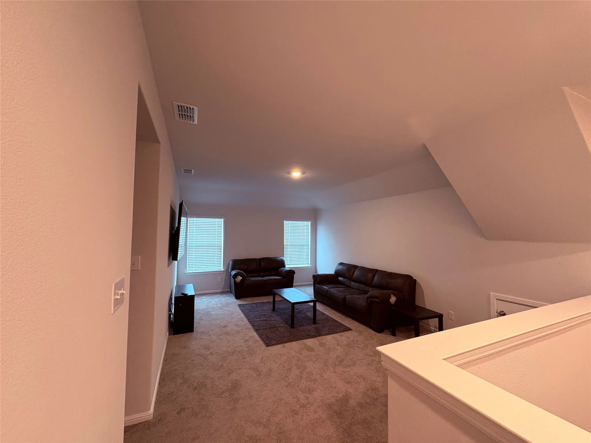 Carpeted living area featuring sloped ceilings, two windows with blinds, and recessed lighting
