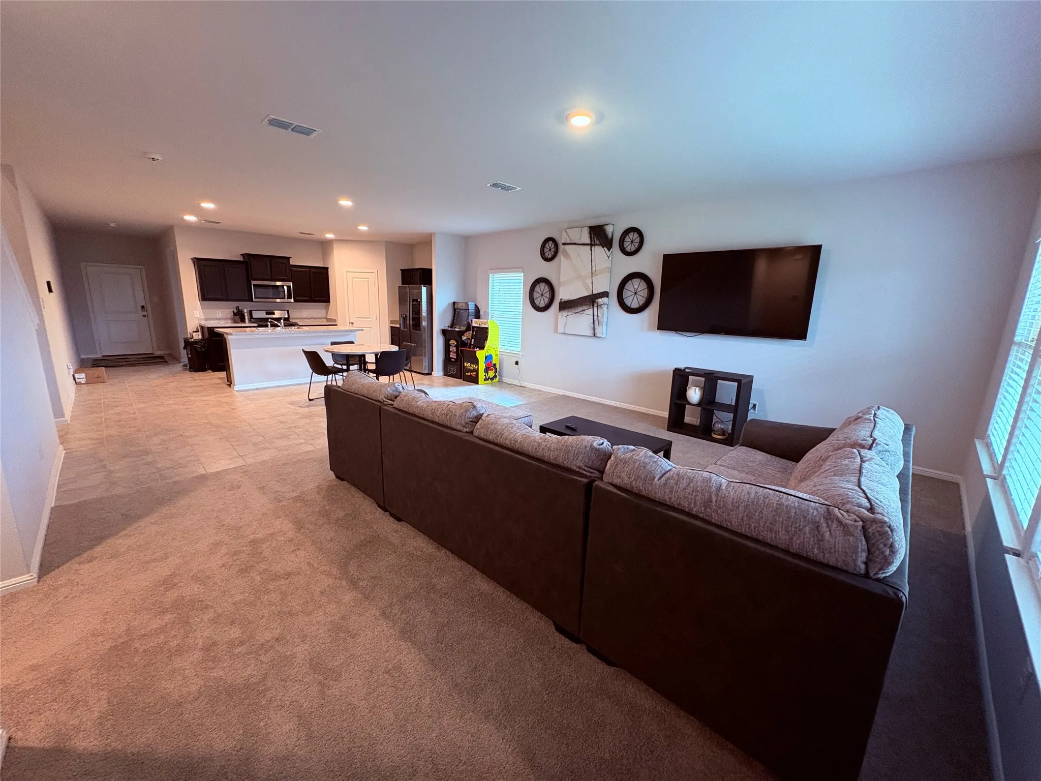 Recessed lighting illuminates the open-concept space, featuring a kitchen with dark wood-finish cabinetry and stainless steel appliances