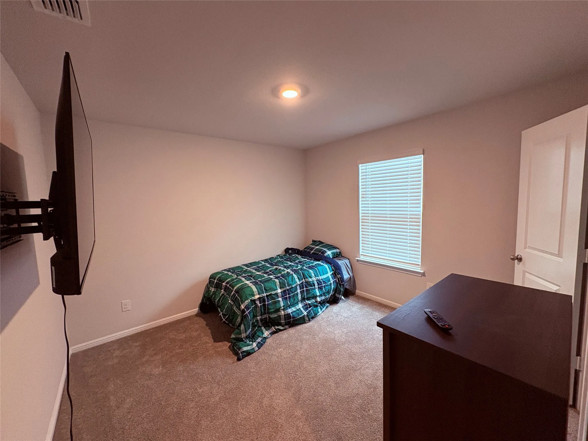 Neutral tone wall color, recessed ceiling lighting, carpeted flooring, window with blinds, and a paneled door with a spherical doorknob