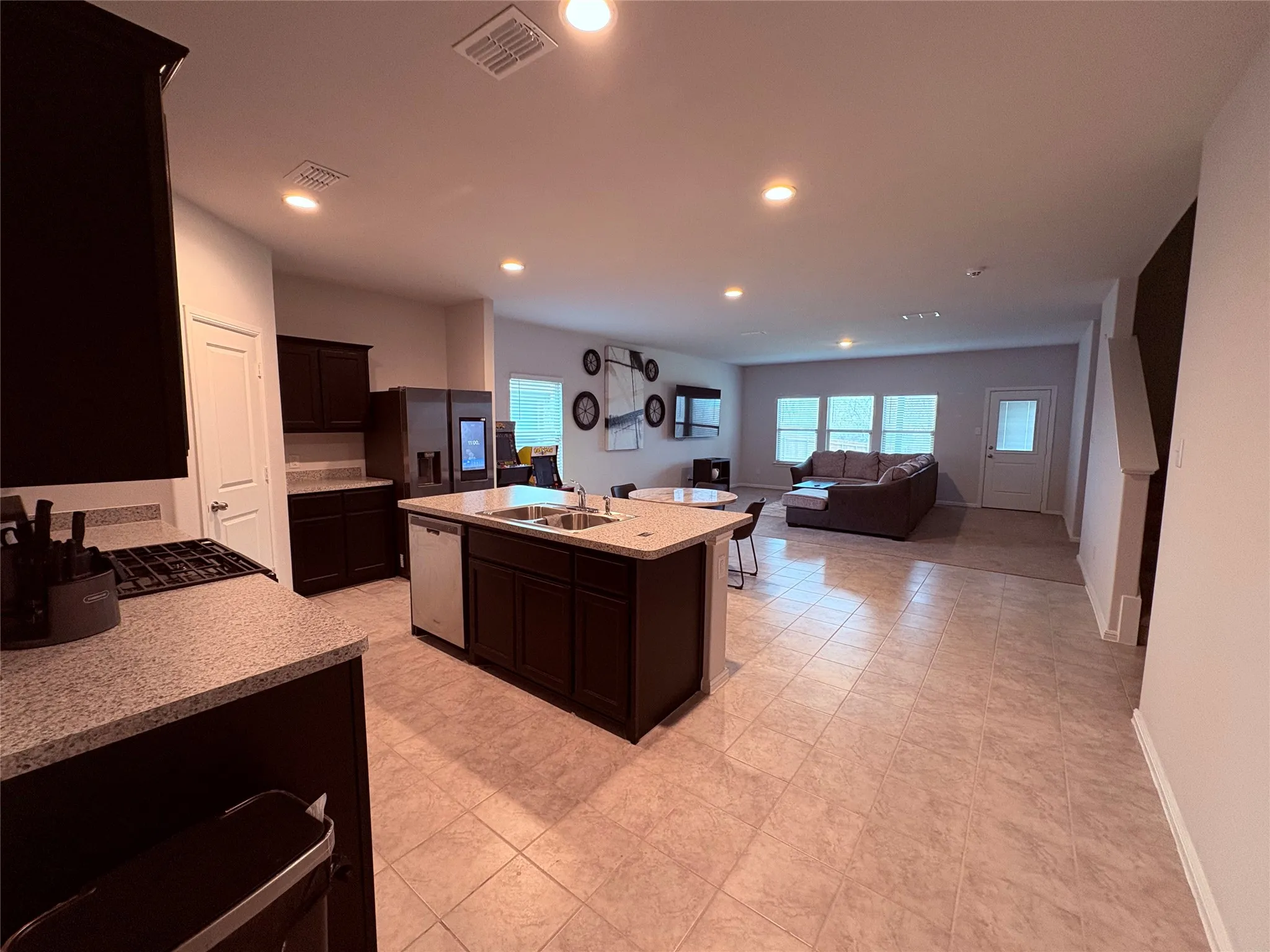 Open-concept living space with dark wood-finish cabinetry, light-toned countertops, and a kitchen island with a built-in sink