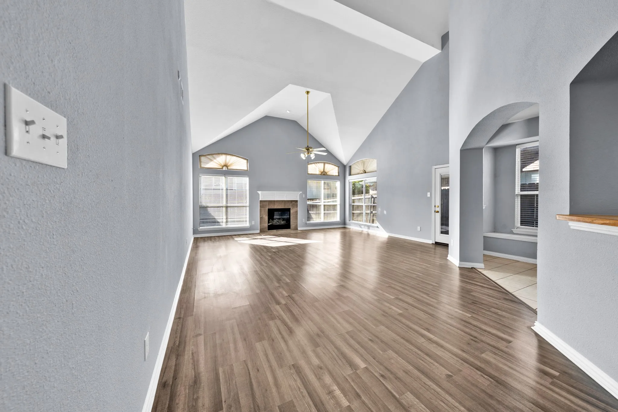 Vaulted ceiling, wood-finish flooring, fireplace with mantel, arched entryway, and multiple large windows