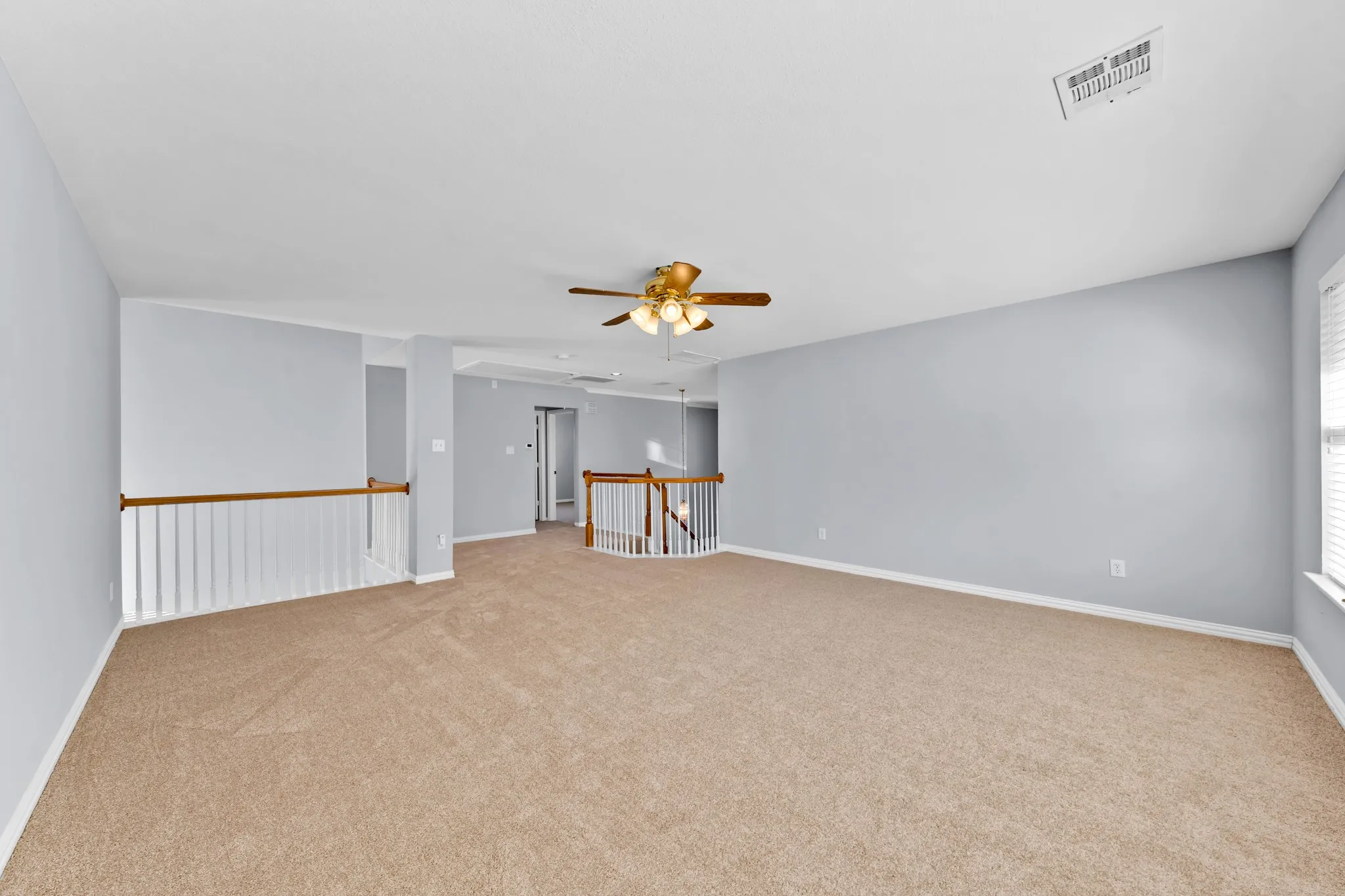 Spacious carpeted room featuring a ceiling fan, light blue walls, white trim, and white railings with wood-finish tops