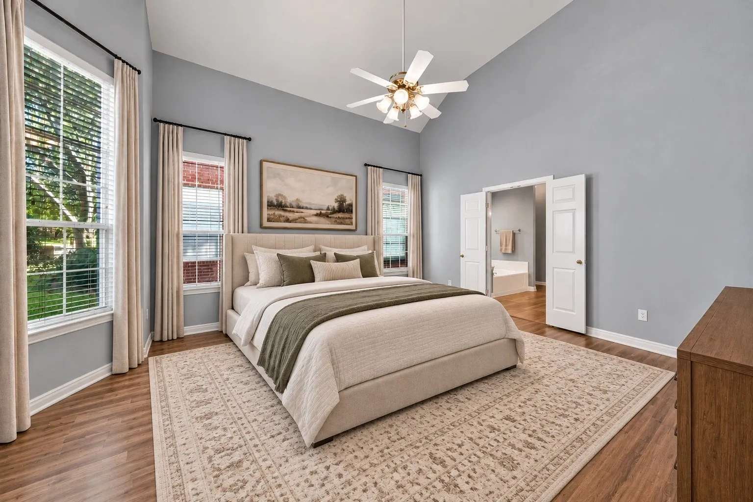 Vaulted ceiling with a ceiling fan, wood-finish flooring, multiple windows, and double doors opening to an adjoining room